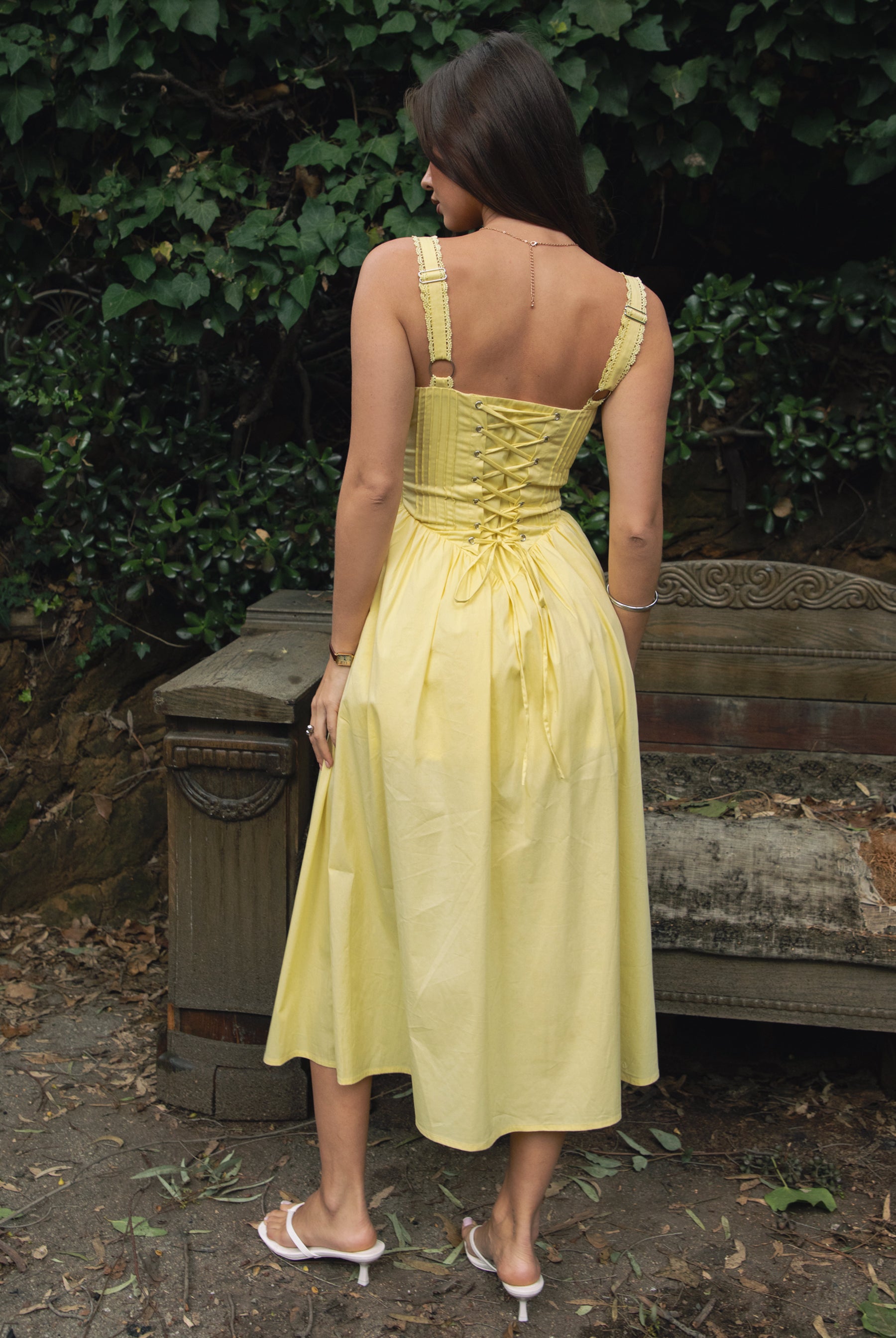 Woman wearing TIC TOC DA31086-LORETTA LORETTA stretch poplin maxi dress featuring adjustable lace shoulder straps, a cinched bust with bow detail, lace overlay corset-style bodice with vertical seaming, lace-up back and hidden side zipper, and a gathered A-line maxi skirt with a shaped waist and V-cut hip seam, styled for a romantic spring/summer occasion look.