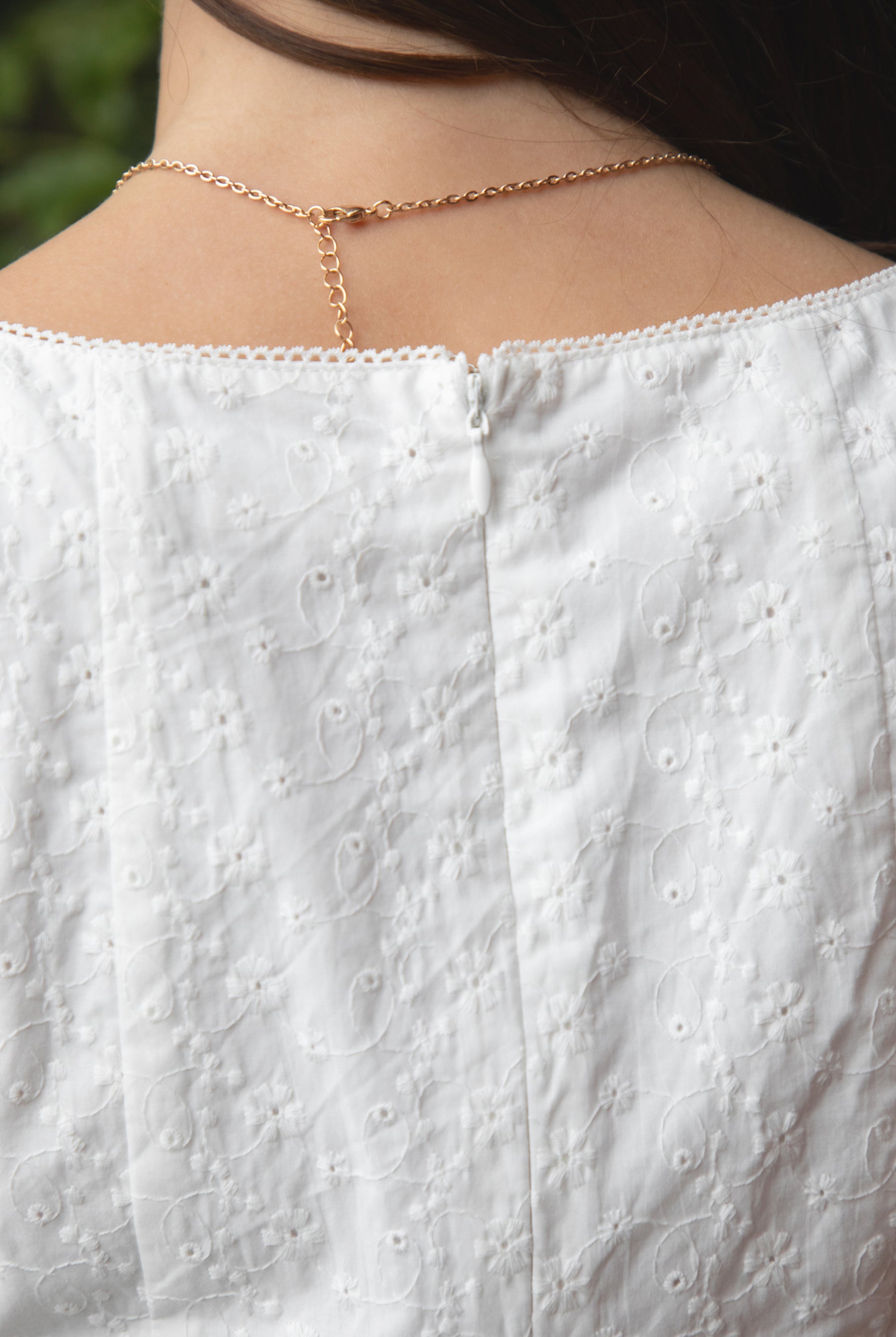 Woman wearing TIC TOC DA31929-AMAYRA AMAYRA eyelet mini dress made from allover eyelet embroidered cotton fabric, featuring a sleeveless square neckline, faux button front detail, fitted bodice with clean seams, adjustable back waist tie, hidden back zipper, and scalloped eyelet lace hemline, styled for a brunch-ready garden party look.