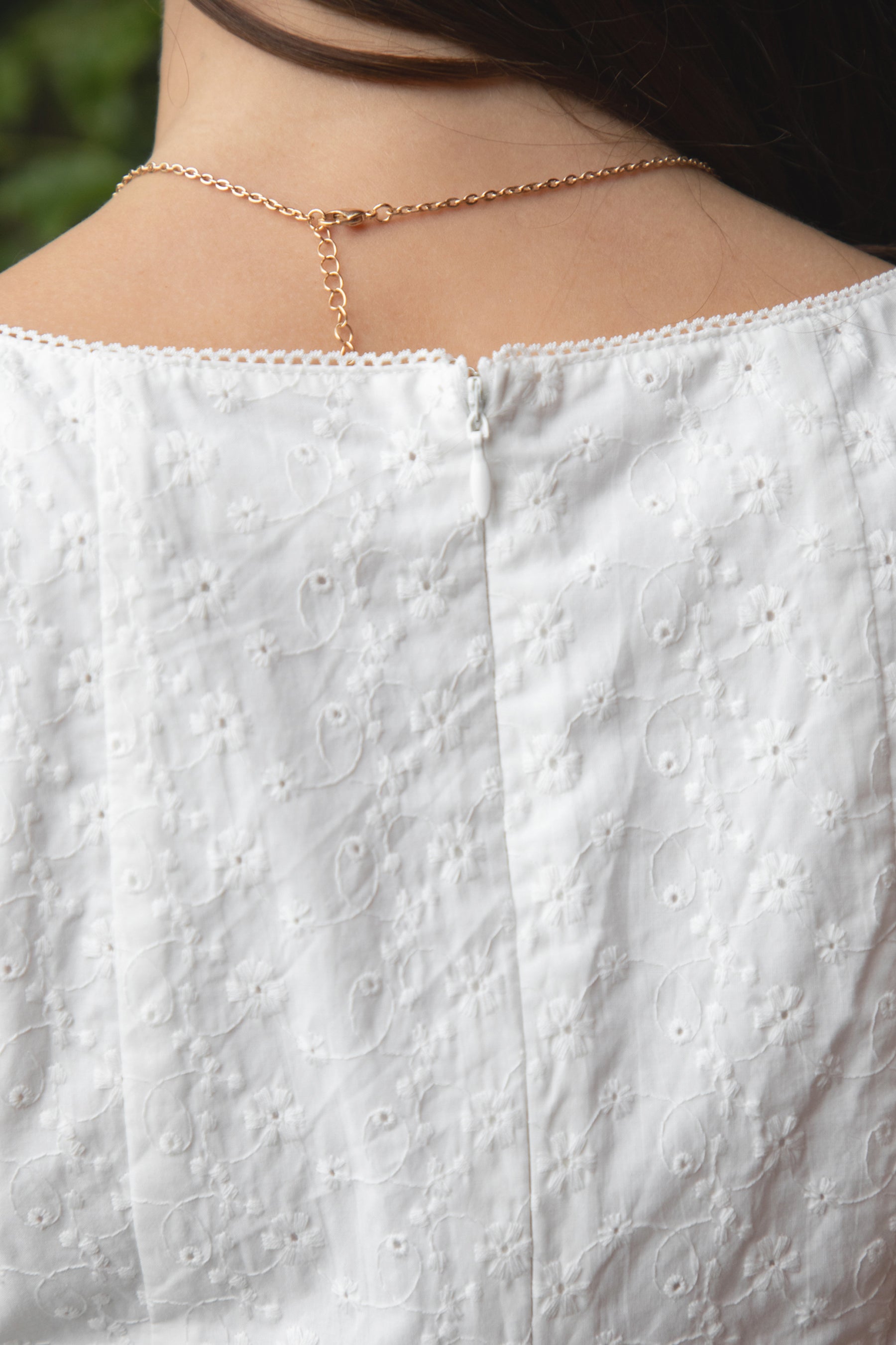 Woman wearing TIC TOC DA31929-AMAYRA AMAYRA eyelet mini dress made from allover eyelet embroidered cotton fabric, featuring a sleeveless square neckline, faux button front detail, fitted bodice with clean seams, adjustable back waist tie, hidden back zipper, and scalloped eyelet lace hemline, styled for a brunch-ready garden party look.