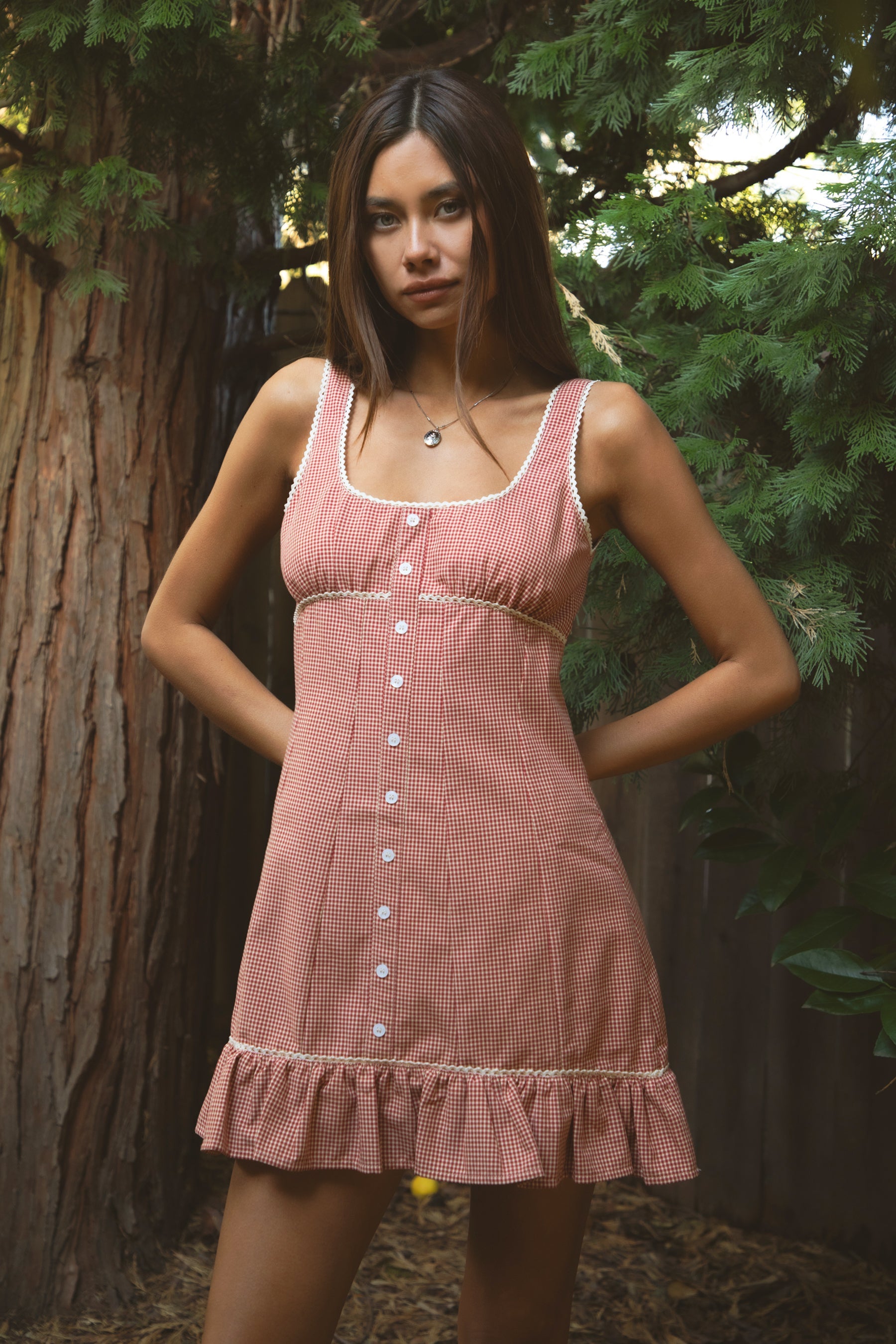 Woman wearing TIC TOC DA31931-AMELIE AMELIE gingham mini dress featuring a square scoop neckline with picot trim, wide shoulder straps, front faux button detail, fitted bodice with under bust seam, ruffled hem mini skirt in gingham poplin fabric, and a clean back zipper closure, styled with simple accessories for a coquette, western-sweet summer look.