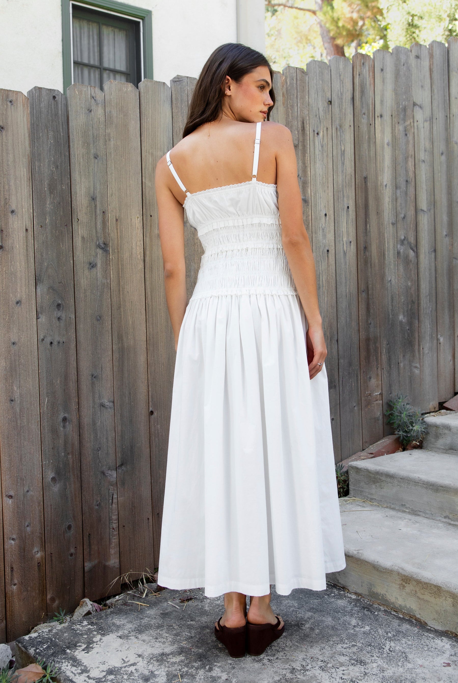 Woman wearing ISLA smocked poplin square neck maxi dress featuring smooth stretch poplin fabric, built in bra cups, straight neckline with ruffle detail, adjustable spaghetti straps, fully smocked bodice, flowing maxi skirt, hidden side pockets, and easy pull on design.
