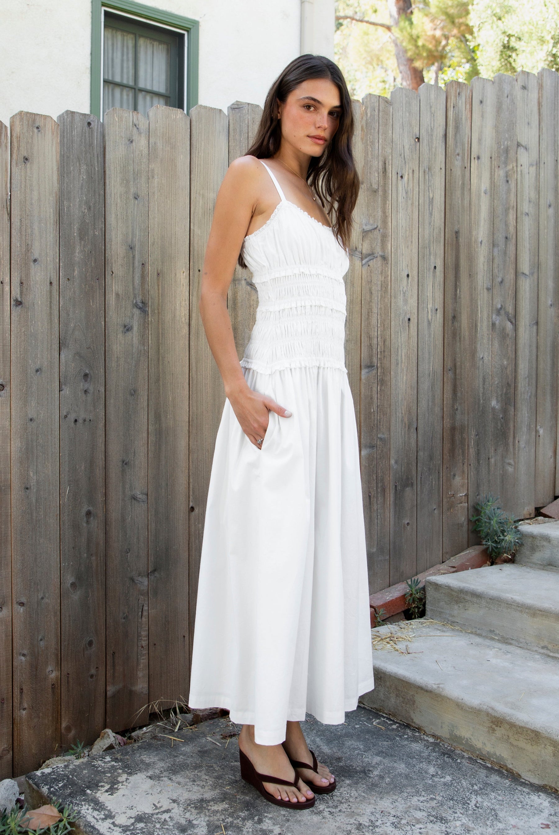 Woman wearing ISLA smocked poplin square neck maxi dress featuring smooth stretch poplin fabric, built in bra cups, straight neckline with ruffle detail, adjustable spaghetti straps, fully smocked bodice, flowing maxi skirt, hidden side pockets, and easy pull on design.