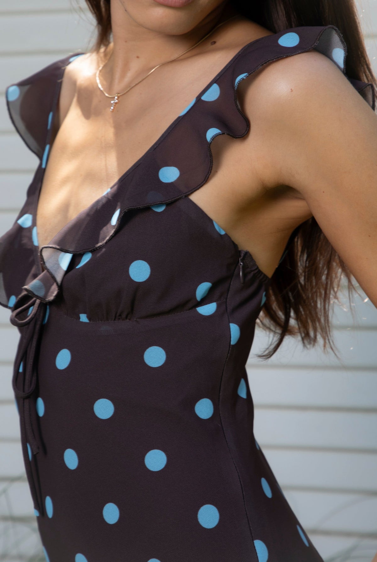 Woman wearing NOIRA ruffle chiffon polka dot maxi dress featuring flowy chiffon fabric, contrast polka dot print, deep V neckline with feminine ruffle trim, ruffled shoulder straps, adjustable front tie detail at the bust, fitted empire waist silhouette, low open back, adjustable shoulder straps, and soft stretch satin lining.