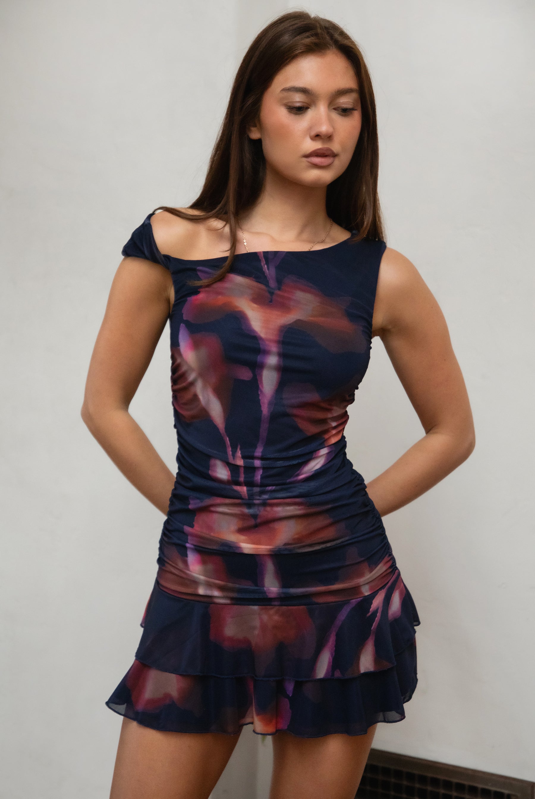 Woman wearing TIC TOC DC31652-VIORELLE VIORELLE mini dress featuring a twisted one-shoulder mesh silhouette with bold graphic print, ruched side detailing, layered ruffle hem mini skirt, and body-hugging fit with a lightweight sheer overlay, styled for a night-out look with heels and minimal accessories.