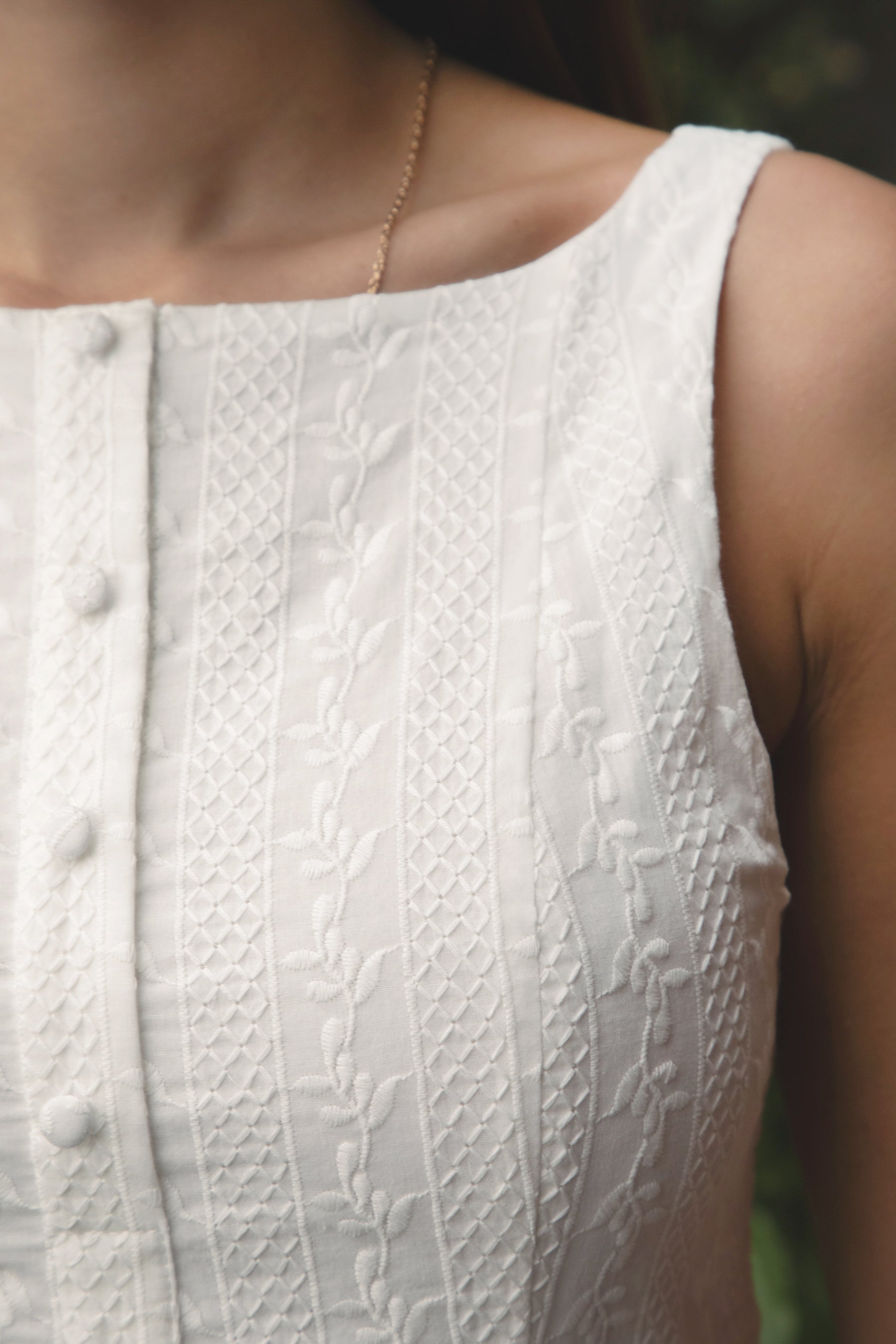 Woman wearing TIC TOC DH31913-AMABEL AMABEL embroidered drop waist mini dress made from allover eyelet embroidered cotton, featuring a clean boat neckline, sleeveless slim fit bodice, faux button front detail, drop waist seam with a flowy mini skirt, open back with zipper closure, and a lightweight fully lined construction, styled for a spring brunch or garden party look.