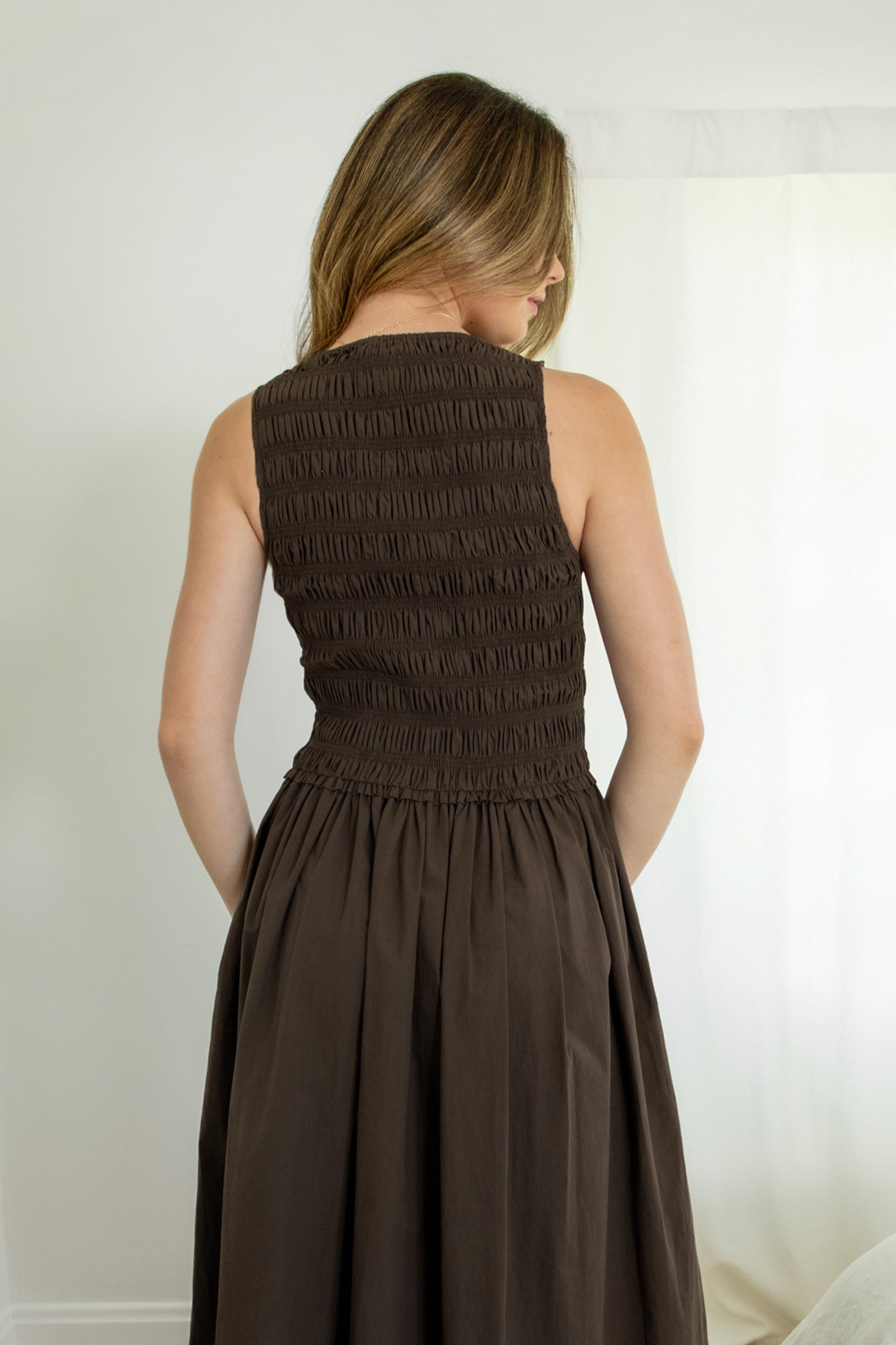Woman wearing BOONE boat neck poplin smocked body midi dress featuring a classic boat neckline, allover smocked bodice, sleeveless silhouette, midi length skirt with soft volume, functional front pockets, and lightweight cotton poplin fabric with a crisp structured feel.