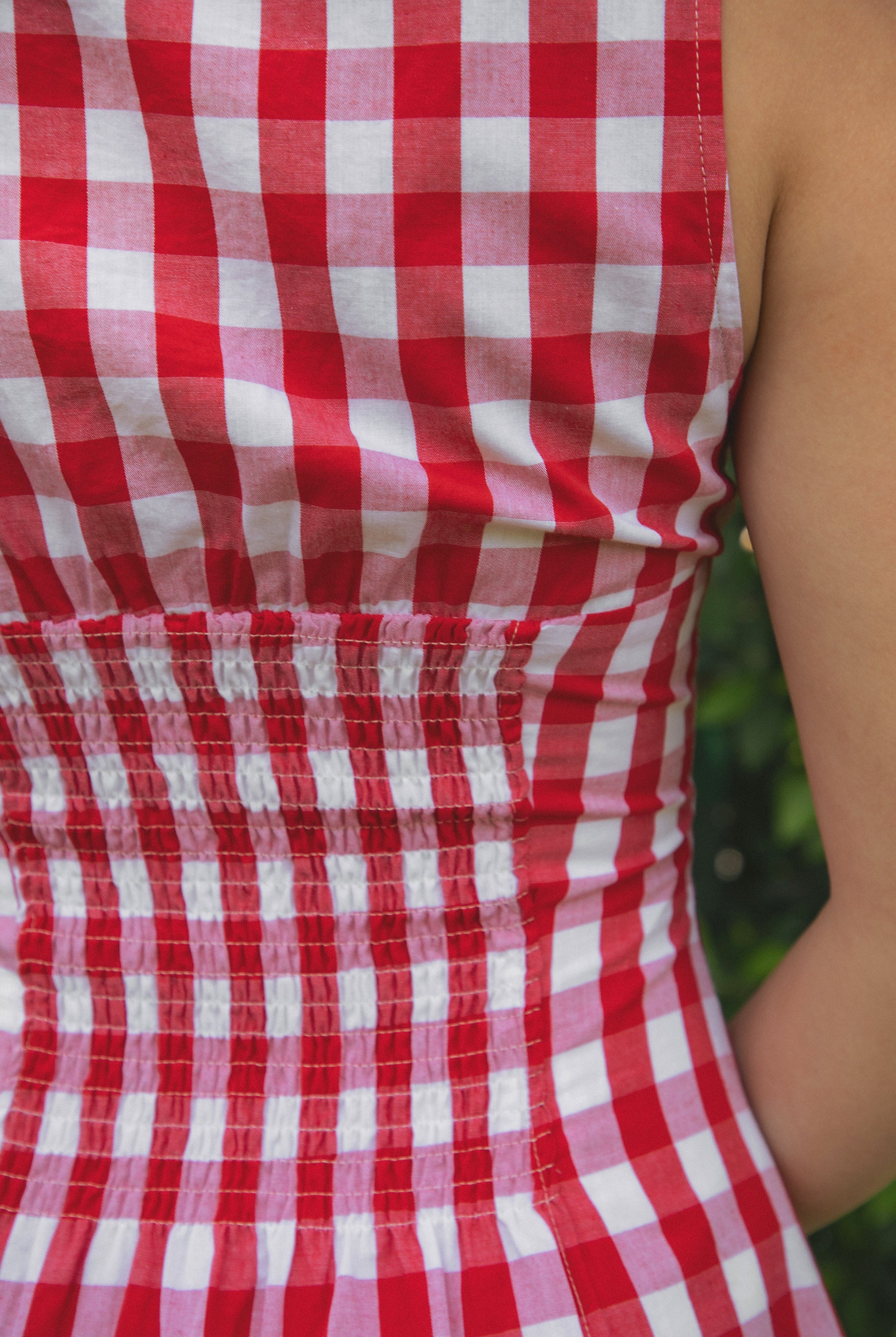 Woman wearing CHERYN V-neck gingham poplin mini dress featuring a classic gingham check pattern, scalloped lace trim neckline, sleeveless fit-and-flare bodice, decorative faux button detail, smocked back panel, hidden side zipper, and floral eyelet lace hem.