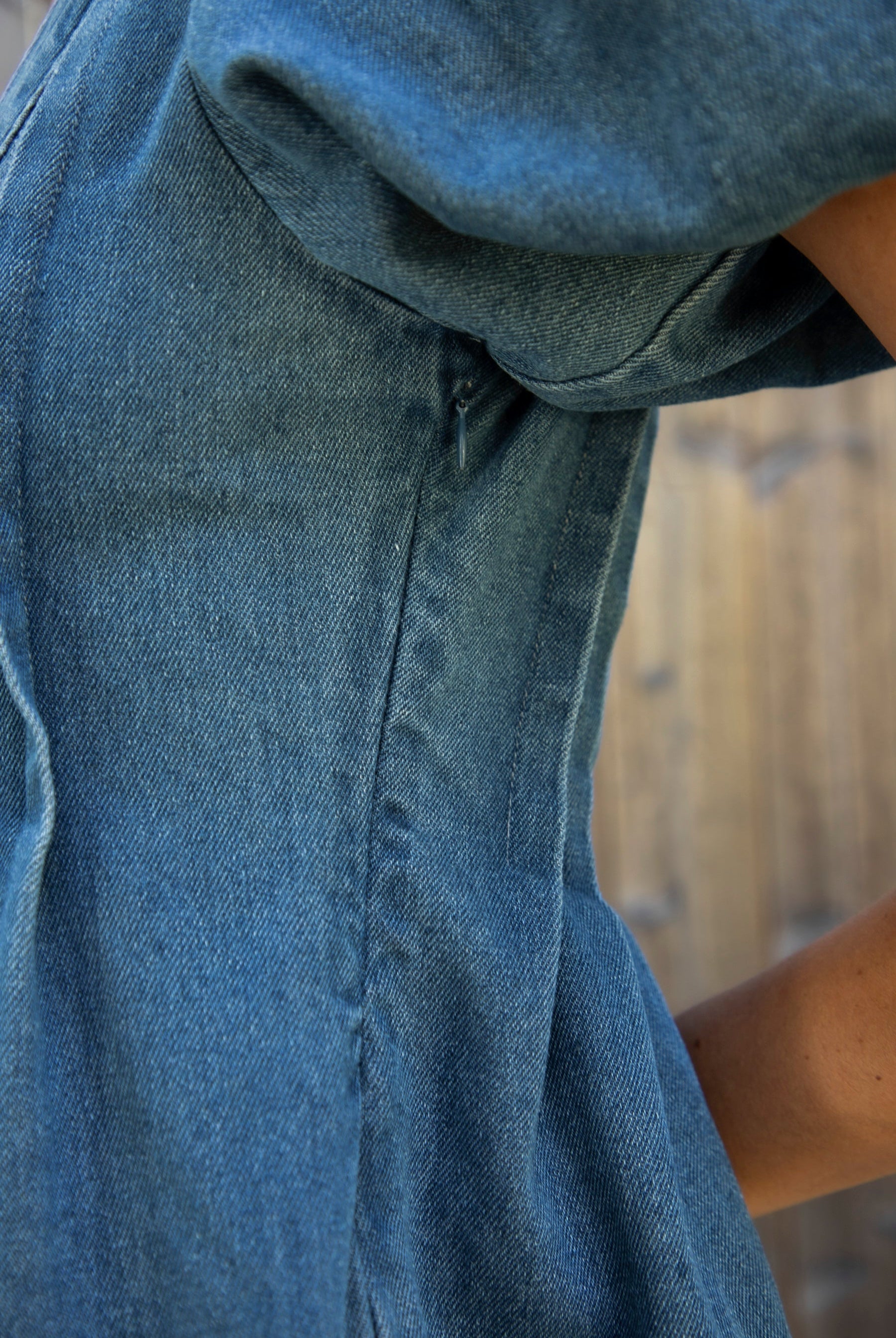 Woman wearing DELANEY soft denim puff sleeve denim romper featuring soft denim fabric, comfortable structured feel, deep V neckline, adjustable front tie detail, statement puff sleeves with gathered volume, pleated bodice, relaxed fit silhouette, and hidden side zipper closure.