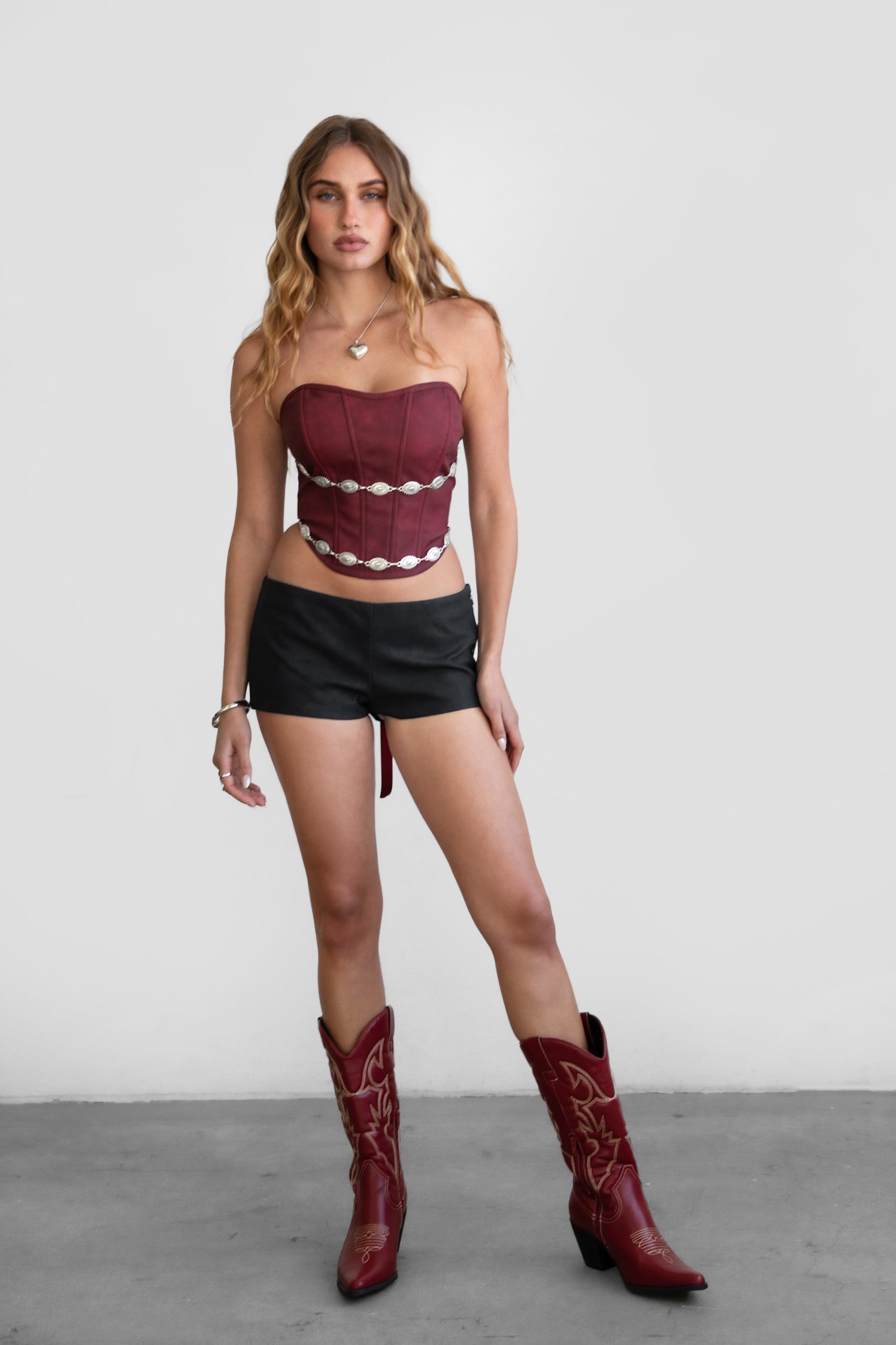 Model wearing LEIAH vegan leather micro shorts in black and brown, styled for a Western festival look