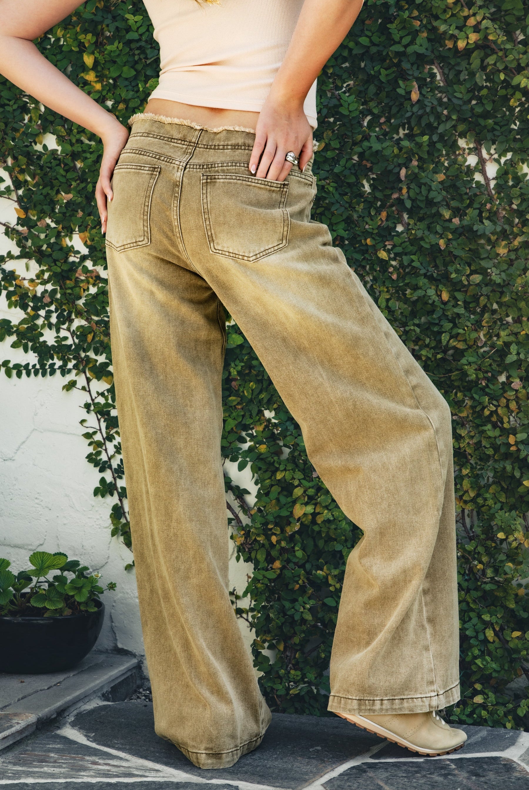 Woman wearing CINDER washed distressed hem wide leg jean featuring a vintage washed denim finish, distressed raw waistband detail, mid rise wide leg silhouette, classic five pocket design, and button and zip front closure for western inspired everyday styling.