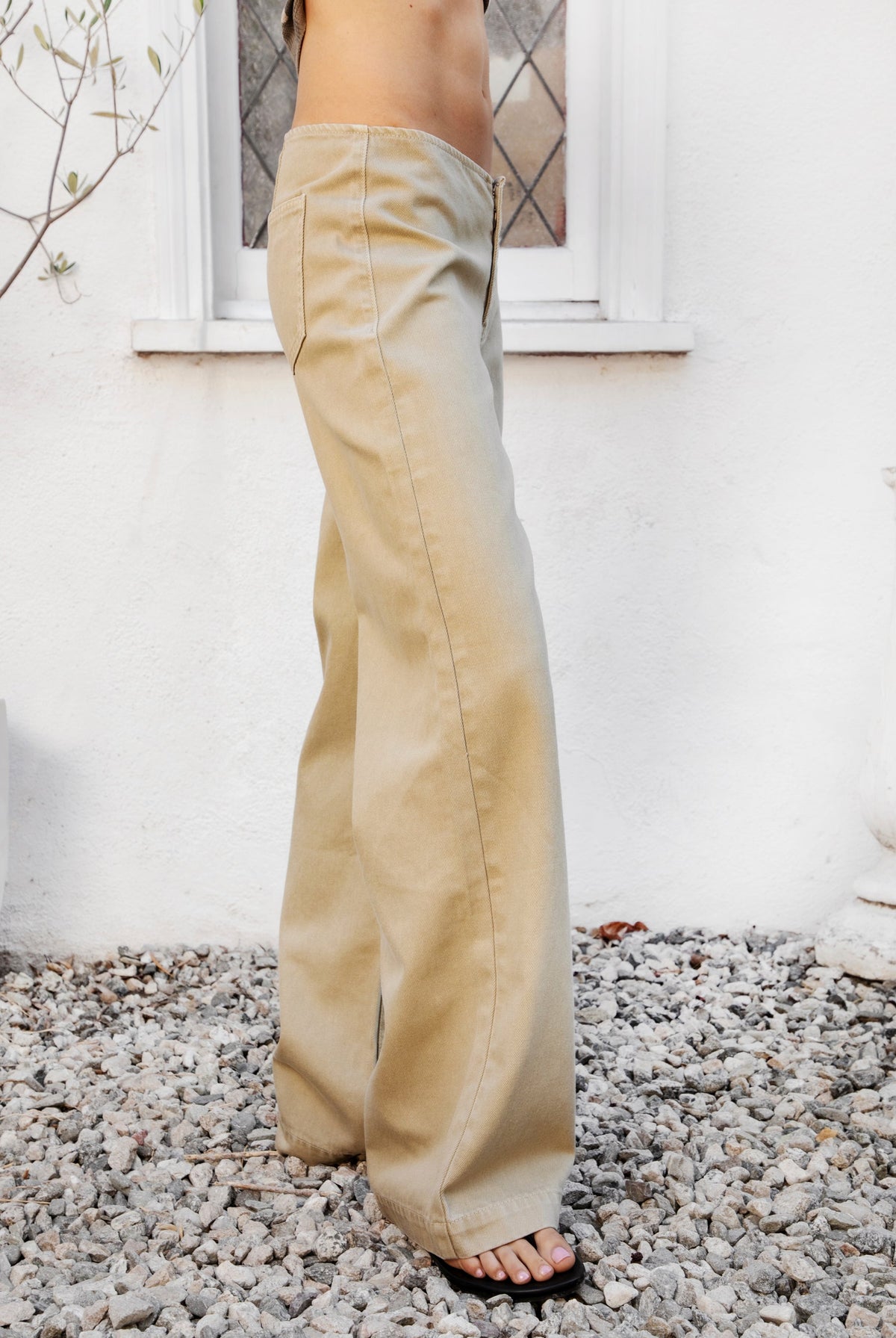 Woman wearing BOWDEN washed low rise wide leg denim pants featuring 100% cotton denim, relaxed vintage inspired silhouette, low rise waist, loose wide leg design, soft lived in washed finish, clean front styling, front zipper fly closure, classic back patch pockets, and full length fit.