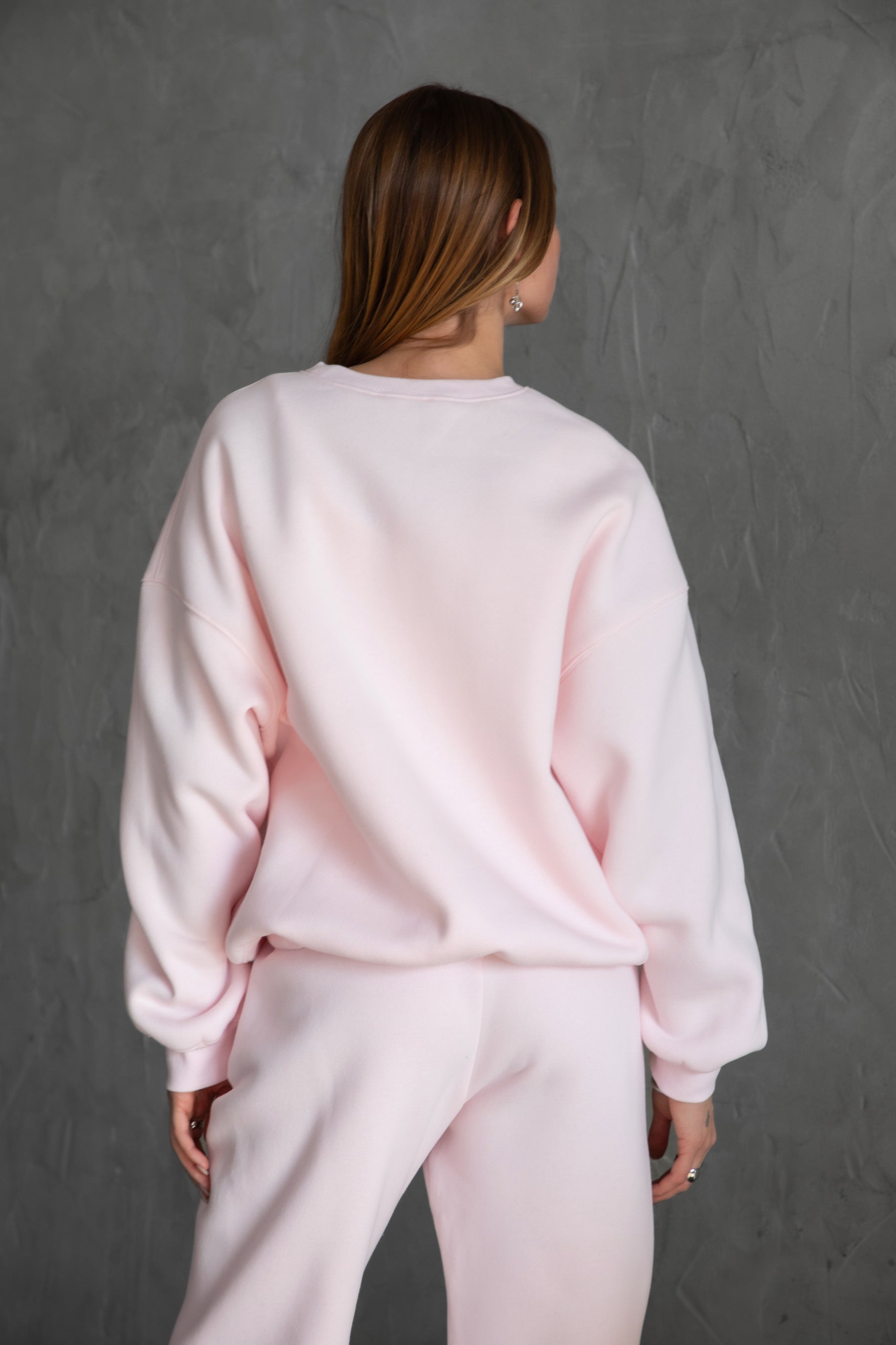 Person wearing a pale pink sweater and pants set on a white background