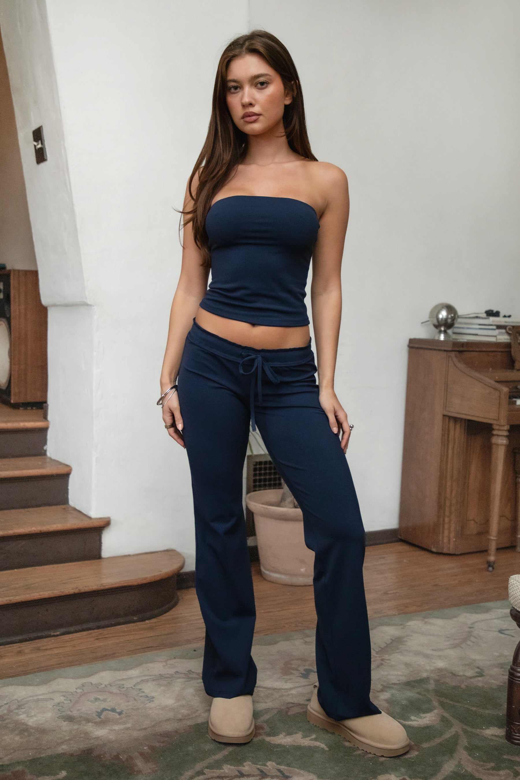 Woman wearing TIC TOC PH31905BA-NYLEE-WL navy NYLEE WL wide leg pants made from soft span jersey fabric, featuring a high-stretch body-hugging fit through the hips, foldover waistband with tie detail, and full-length wide leg silhouette, styled indoors with a matching top for a coordinated lounge/athleisure look.