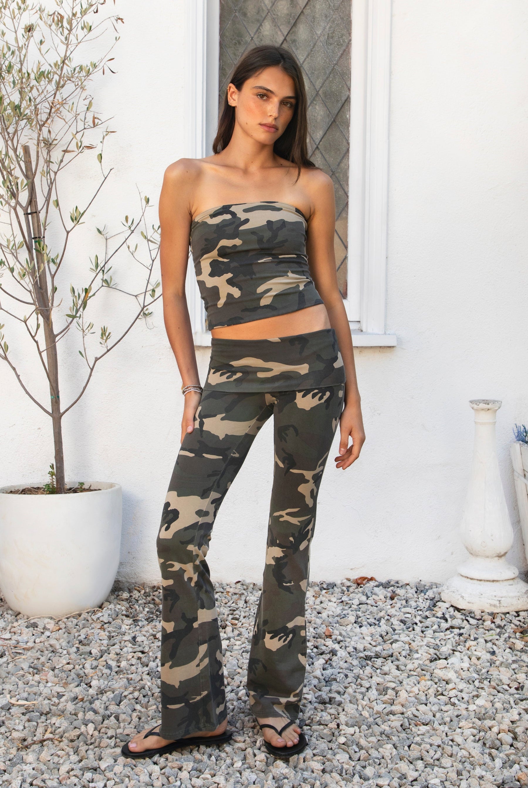 Woman wearing REMI dark military camo fold over flare leggings featuring soft stretch cotton jersey fabric, allover classic military camouflage print, low rise fit, wide fold over waistband, fitted hips and thighs, flared leg, garment washed finish, and full length pull on silhouette.