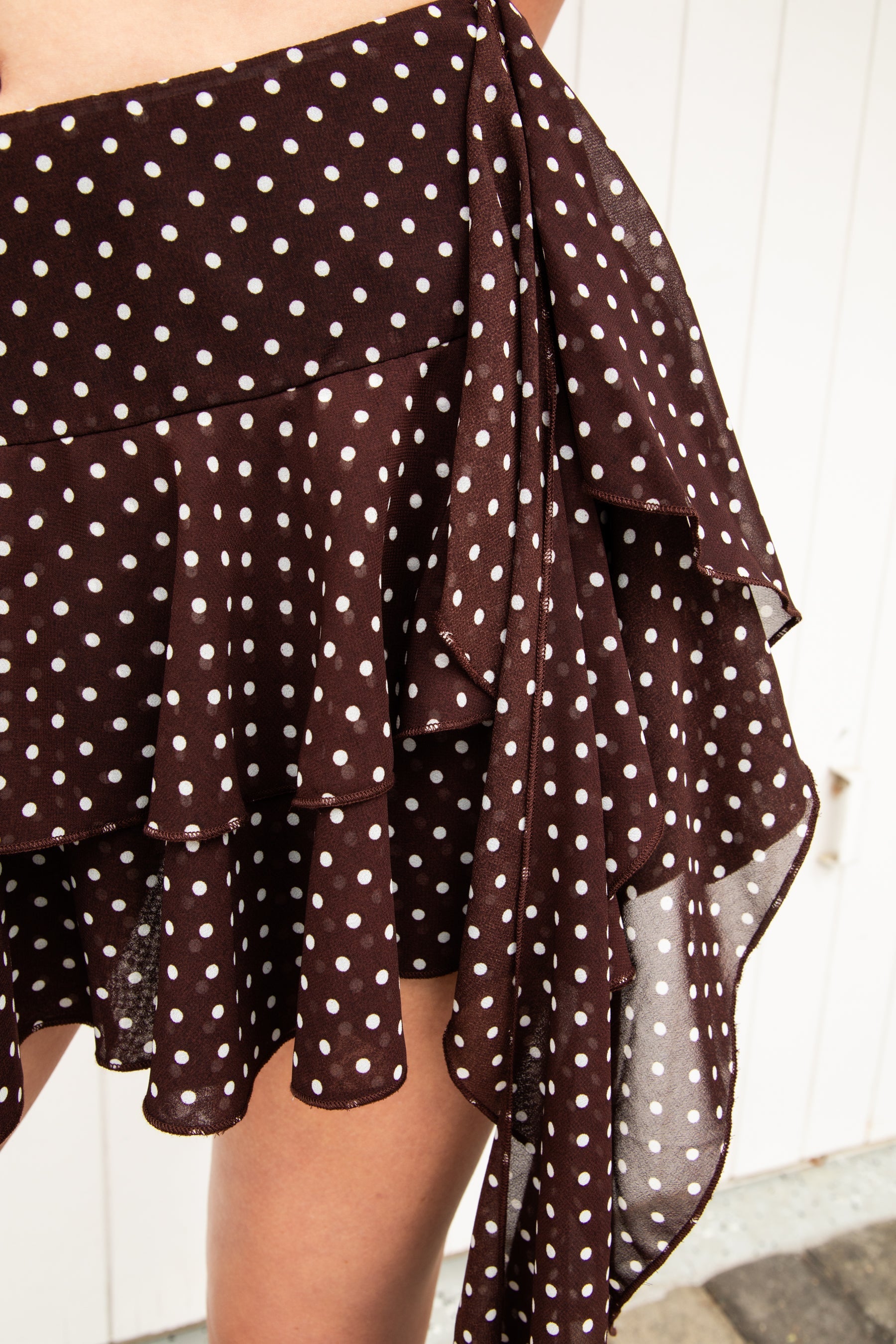 Woman wearing BISCOTTI polka dot chiffon ruffle skirt featuring a tiered mini skirt silhouette, asymmetrical dropped ruffle side detail, side zipper closure, built-in shorts lining, and a lightweight flowy hem for coquette summer and resort styling.