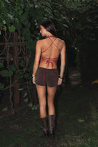 Woman in a strappy top and shorts walking outdoors with greenery in the background