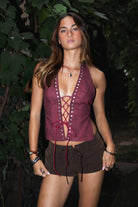 Woman wearing a burgundy top with lace-up front and brown shorts outdoors.