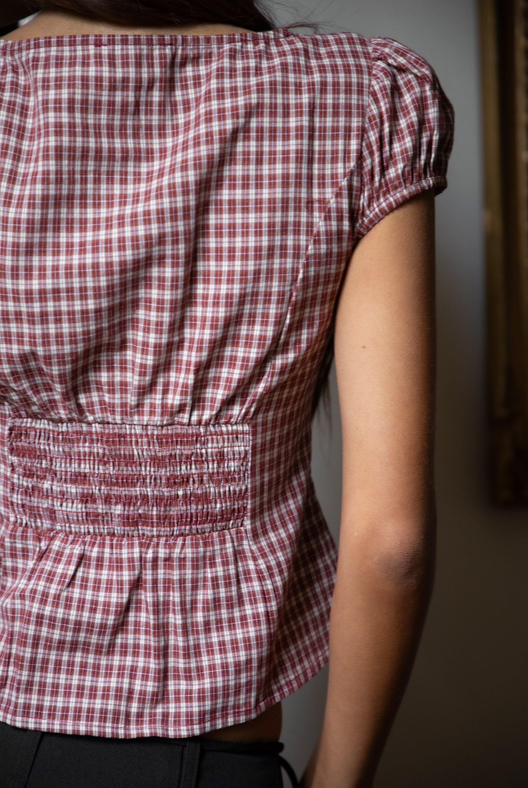 Woman wearing TIC TOC TA32072 DARIS gingham puff sleeve blouse top featuring soft cotton gingham fabric with a classic check pattern, cropped feminine fit, round neckline with front button closure, puff short sleeves, smocked back panel, and under bust smocking for a vintage-inspired western look.