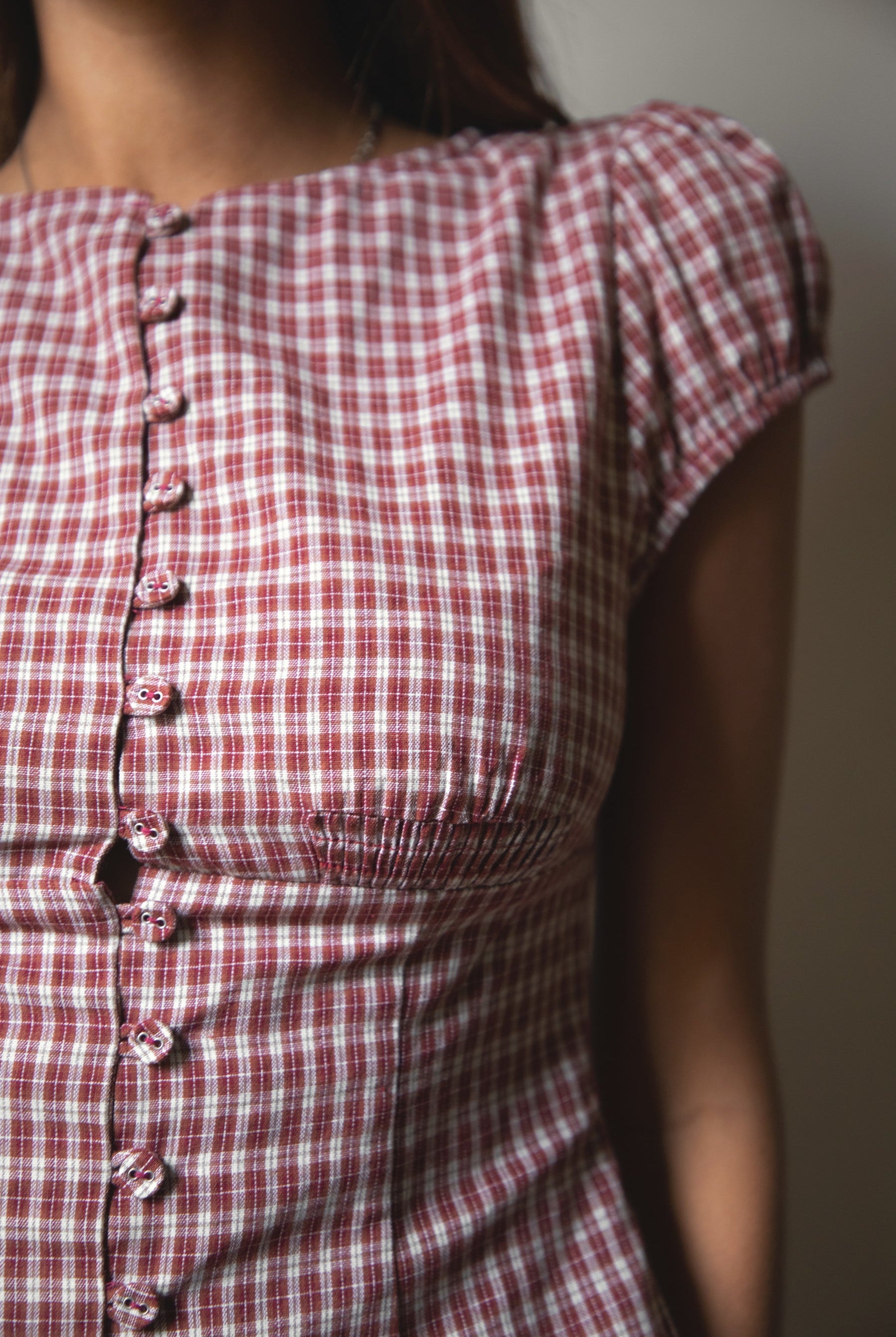 Woman wearing TIC TOC TA32072 DARIS gingham puff sleeve blouse top featuring soft cotton gingham fabric with a classic check pattern, cropped feminine fit, round neckline with front button closure, puff short sleeves, smocked back panel, and under bust smocking for a vintage-inspired western look.