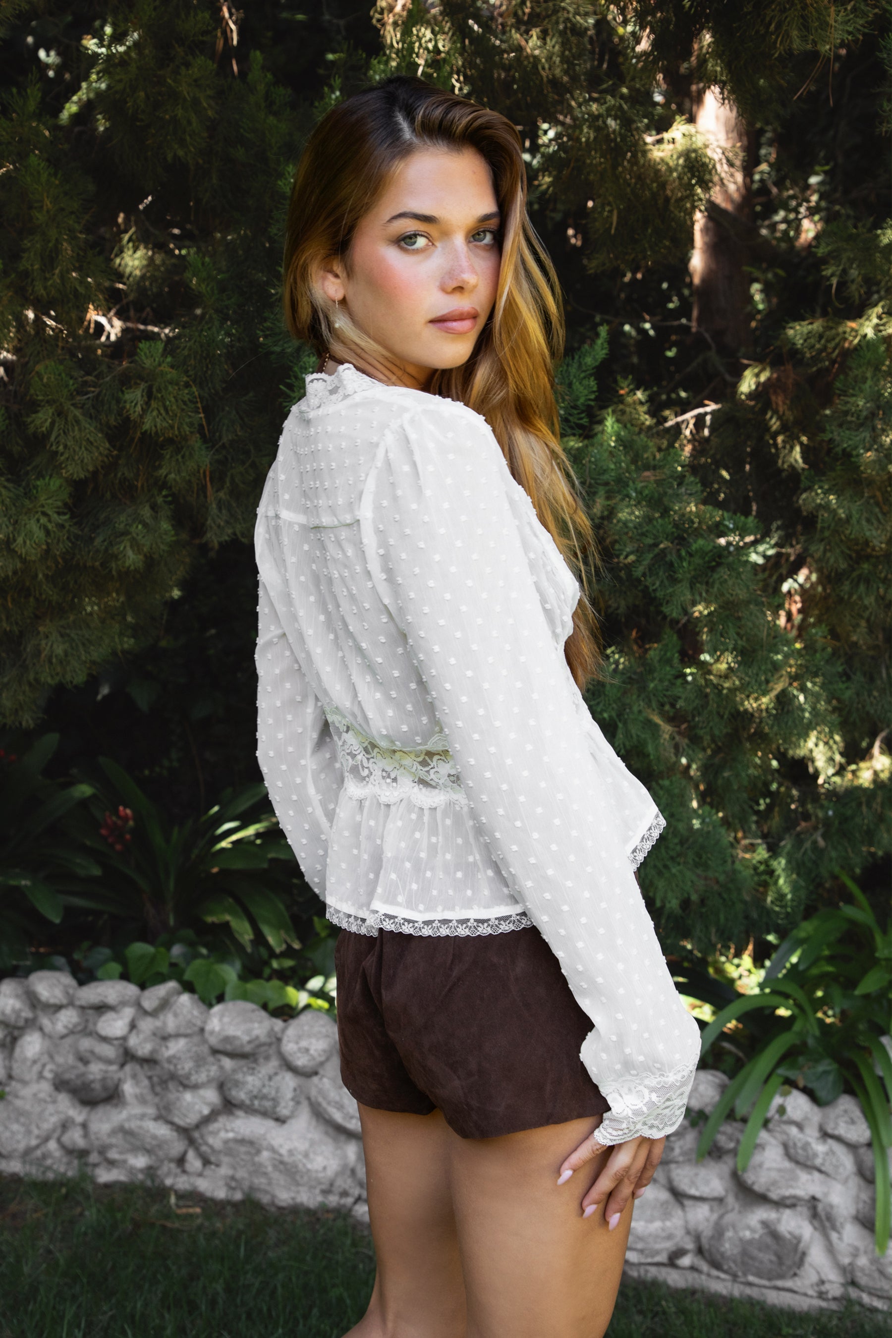 Woman wearing LACEWOOD polka dot chiffon lace long sleeve blouse top featuring sheer dotted chiffon fabric, scalloped lace trim along the V-neckline and cuffs, floral lace panel under the bust, flowy silhouette with flare hem, and front button closure for adjustable styling