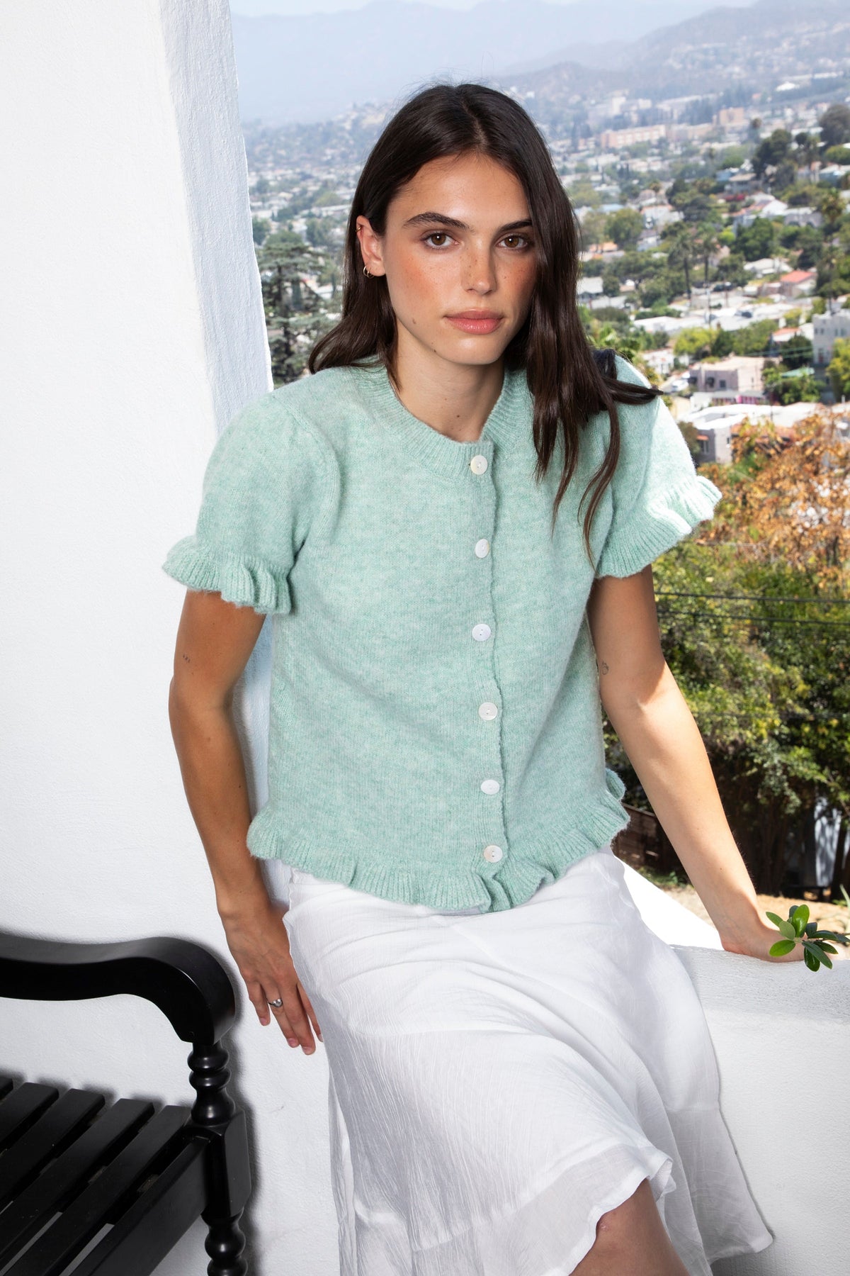 Woman wearing ELSSEE soft ruffle trim button down knit cardigan featuring soft brushed sweater knit fabric, classic crew neckline, button front closure, short puff sleeves with delicate ruffle cuffs, ruffle trim hem, and a cozy cropped silhouette for everyday layering.