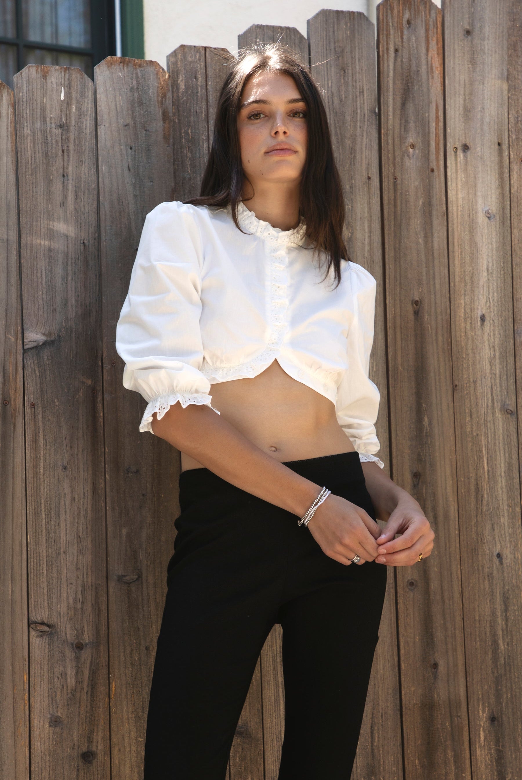 Woman wearing MAIZY eyelet trim cropped three quarter sleeve poplin blouse featuring lightweight cotton poplin fabric, romantic high ruffle neckline, delicate eyelet lace trim, open front cropped silhouette, voluminous puff sleeves, elastic ruffle cuffs, and elasticized hem for feminine styling.