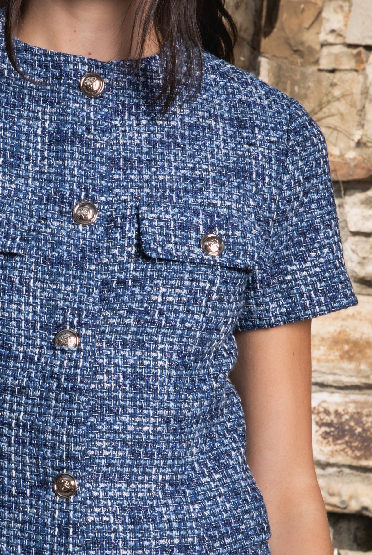 Woman wearing COCO navy blue lurex tweed short sleeve top featuring shimmering textured tweed fabric, subtle metallic lurex detail, round neckline, fitted structured bodice, cropped length, elegant gold point buttons, decorative faux chest pockets, and fully lined construction designed to coordinate with the matching COCO skort.
