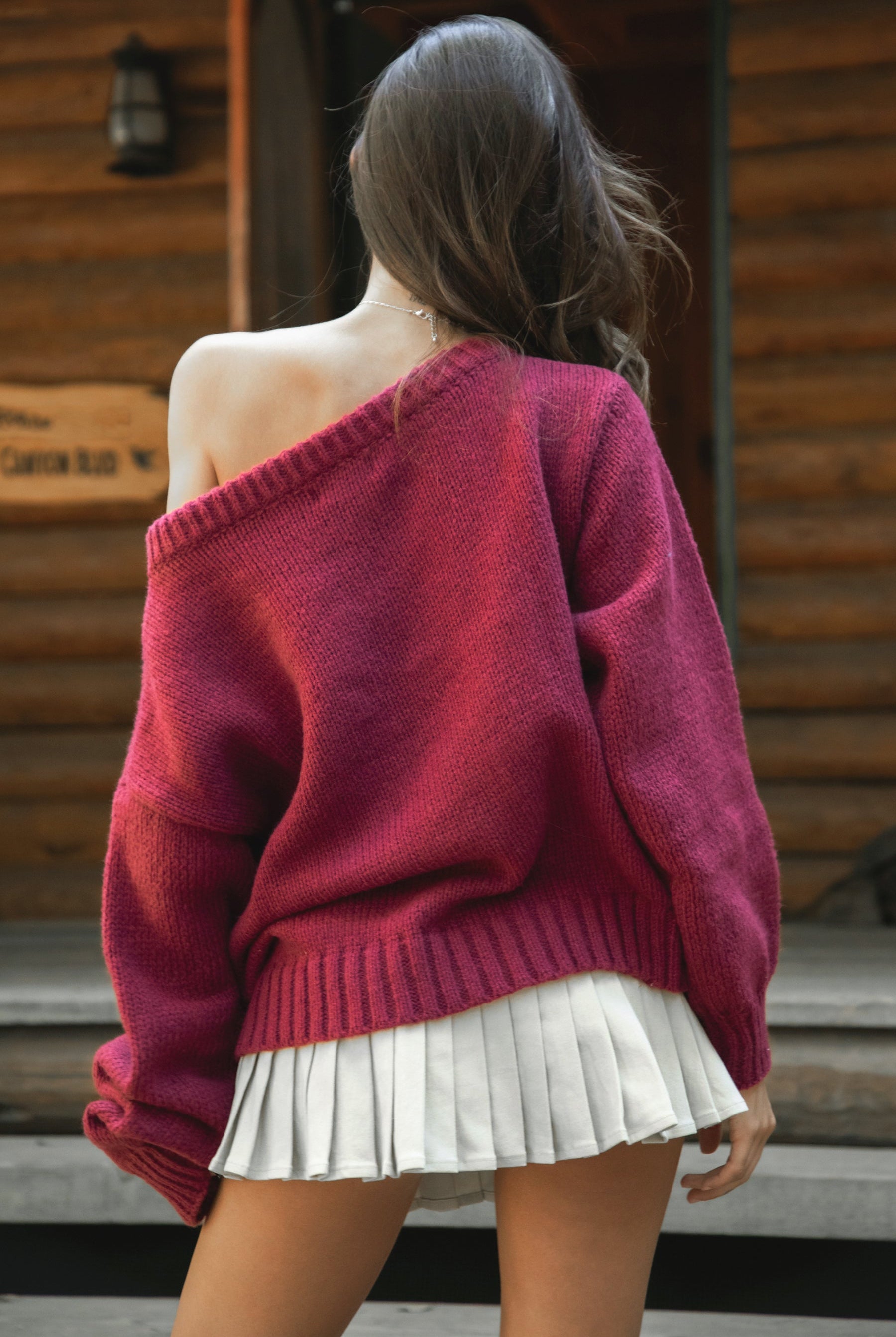 Woman wearing a TIC TOC BRANDI Ribbed Knit Sweater in red with off-the-shoulder boat neck, American flag pattern, and semi-oversized fit, paired with pleated khaki skirt and green rain boots standing on wooden steps.