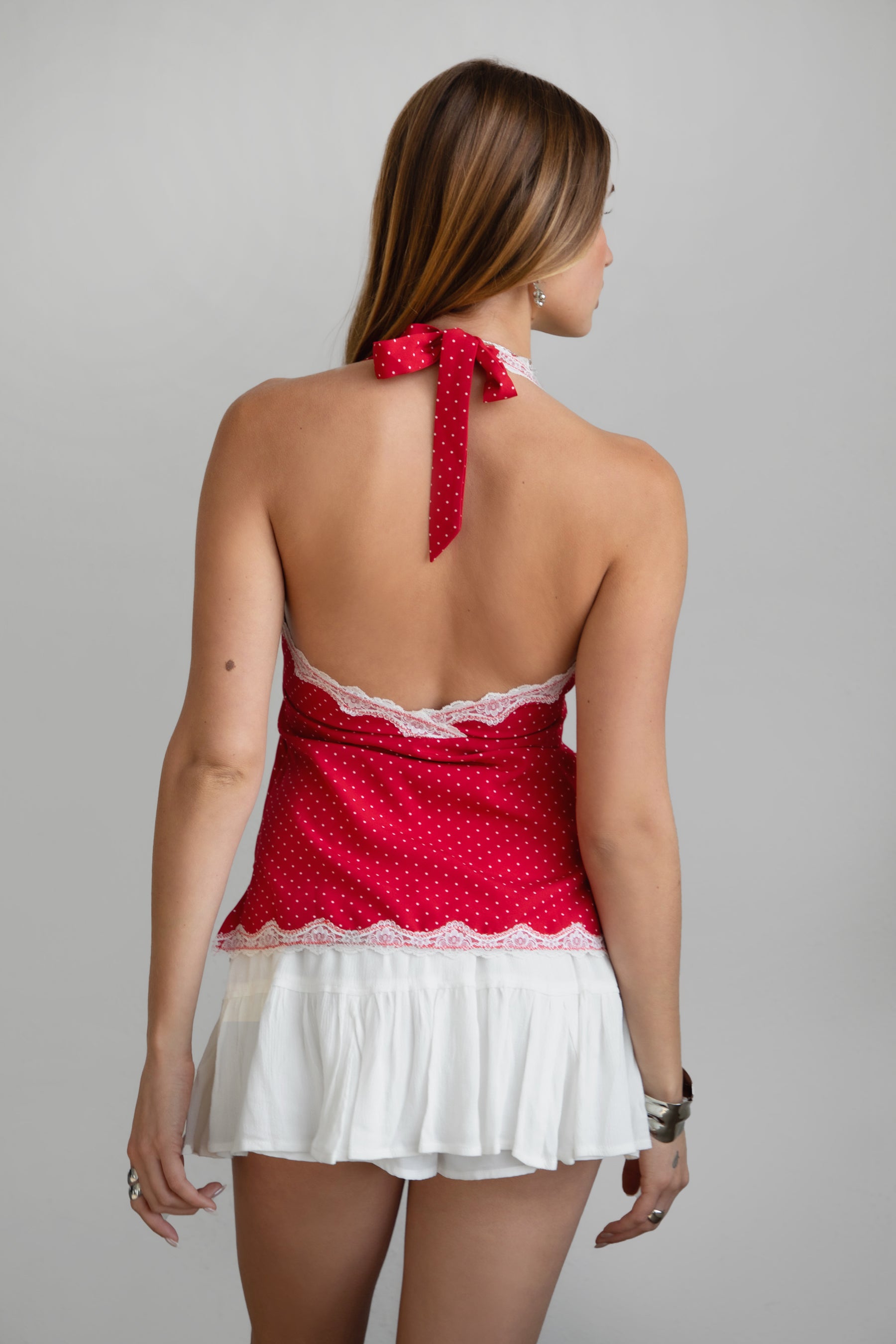 Woman wearing a red polka dot top with a white skirt on a gray background