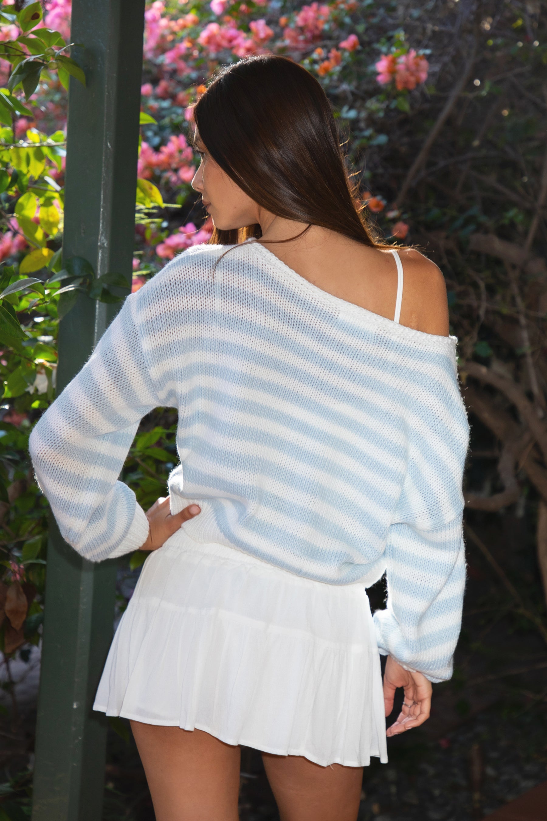 Woman wearing TIC TOC TC31201 PAISEY striped knit off the shoulder oversized sweater with rugby color block pattern inblush and cream paired with a white mini skirt in an outdoor setting.