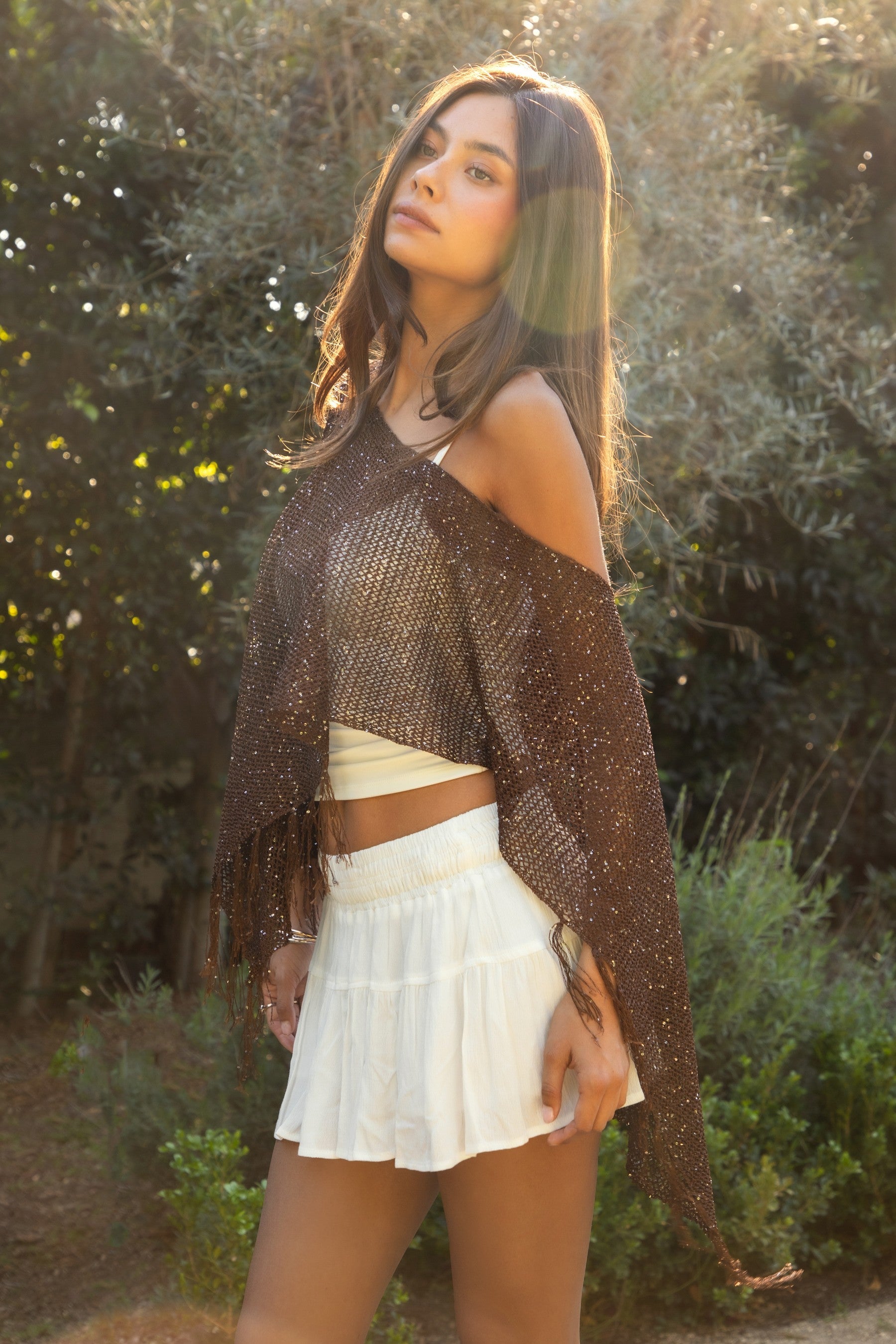 Woman wearing TIC TOC TC31650-SOLENA SOLENA crystal sequin crochet poncho featuring lightweight open crochet knit fabric, allover crystal sequin embellishments, a wide off-shoulder neckline, relaxed draped poncho silhouette, cropped asymmetrical hem, and thin tassel fringe detail, styled over a fitted inner layer for a western festival and vacation-ready look.