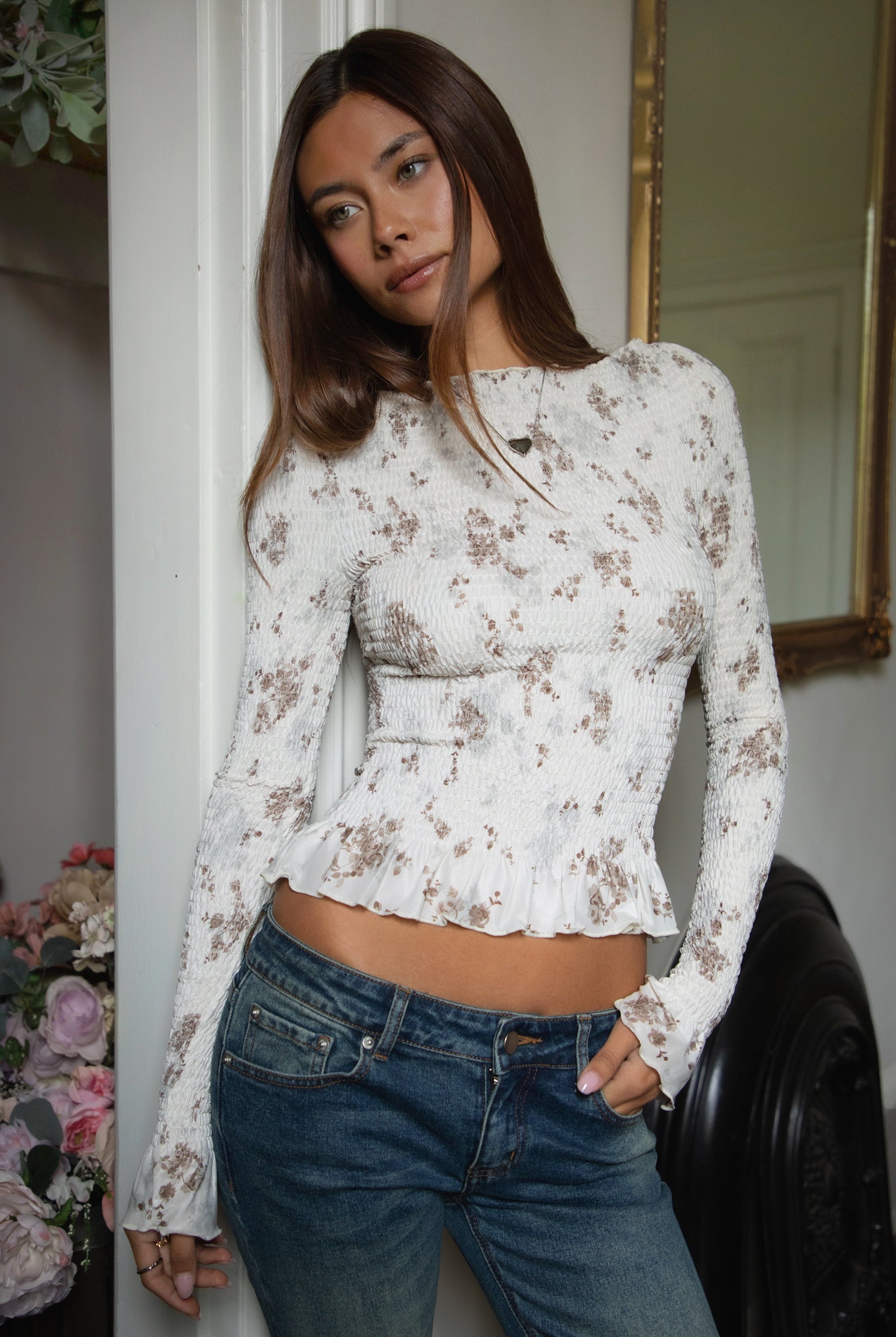 Woman wearing TIC TOC TC31955 MAEVA boat neck mesh print smocked long sleeve top featuring soft stretch smocked fabric with an allover floral print, cropped body-hugging fit, high boat neckline, and long sleeves with subtle ruffle hem and cuffs for a romantic modern western-inspired look.