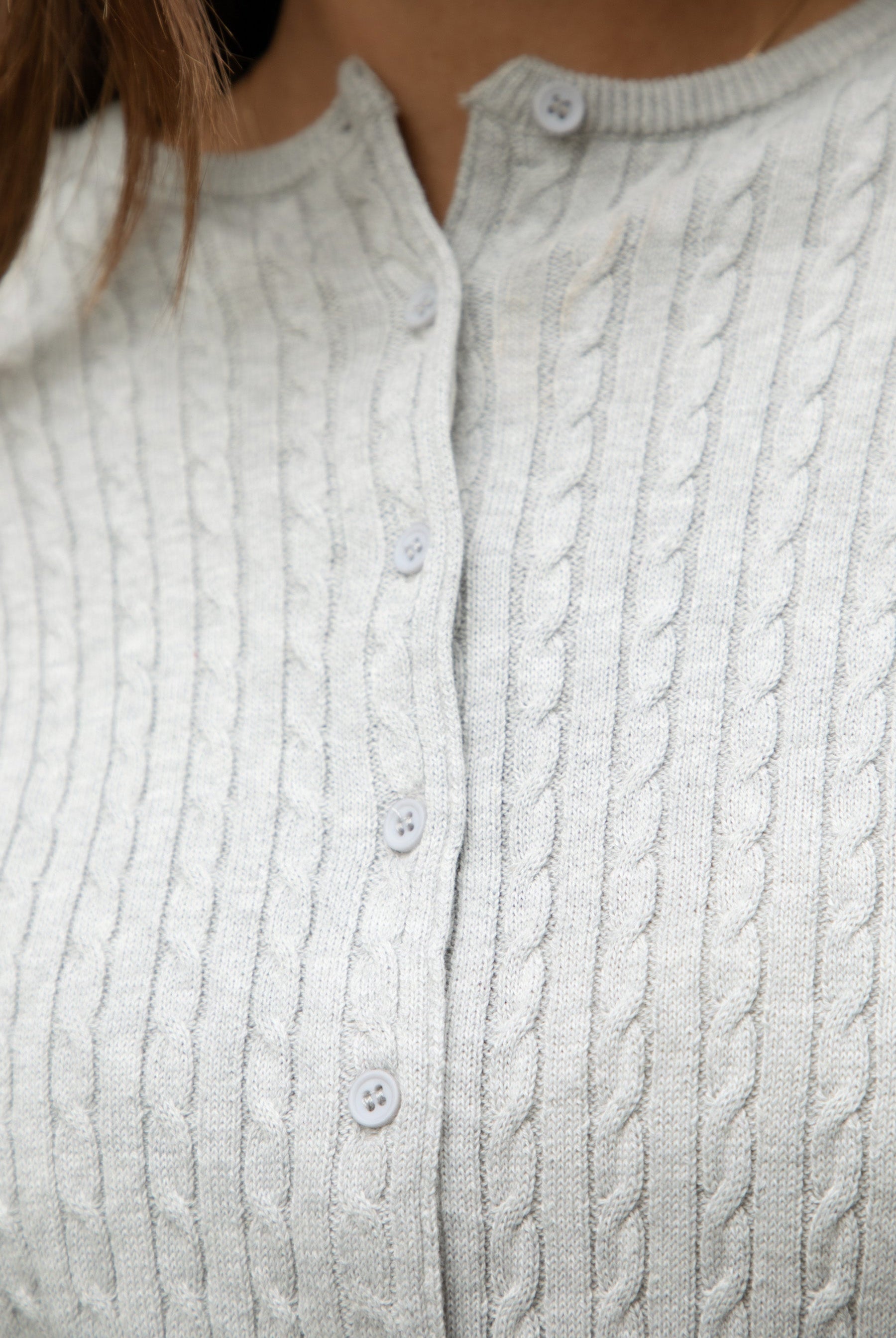 Woman wearing TIC TOC TC32069 KRISTY cable knit basic long sleeve cardigan top featuring a soft lightweight cotton cable knit texture, round neckline, full front button closure, slim fit silhouette, and semi-cropped length for a polished preppy everyday look.