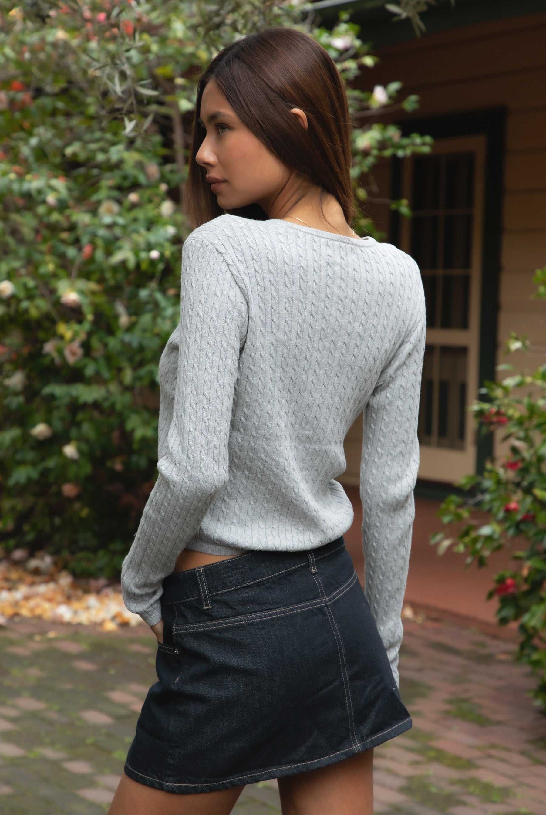 Woman wearing TIC TOC TC32069 KRISTY cable knit basic long sleeve cardigan top featuring a soft lightweight cotton cable knit texture, round neckline, full front button closure, slim fit silhouette, and semi-cropped length for a polished preppy everyday look.