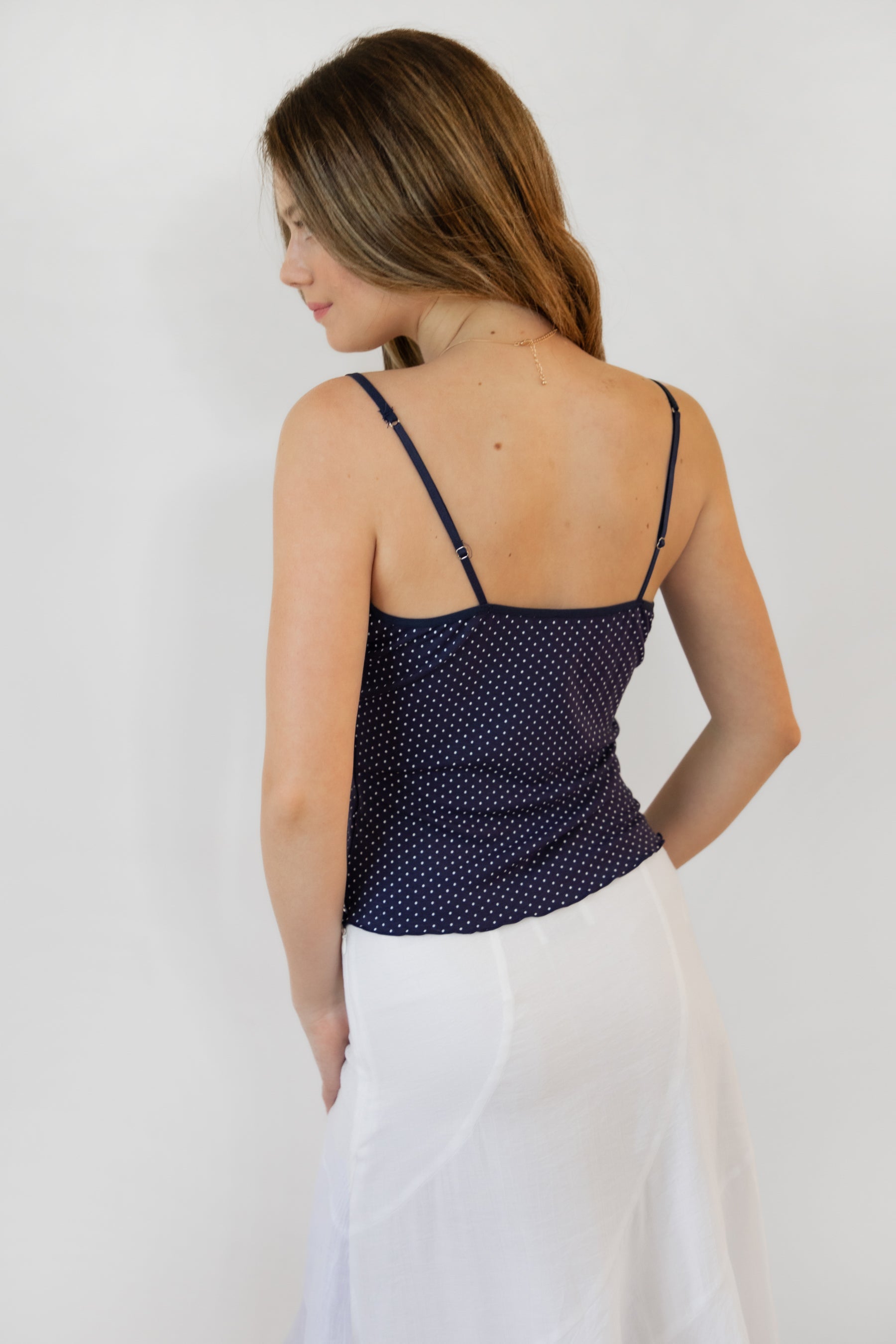 Woman wearing LOTTIE polka dot print lace contrast jersey tank featuring a delicate polka dot print, V-neckline with self-tie bow detail, lace trim along the neckline and under bust, adjustable thin straps, and a soft stretch jersey body-skimming silhouette.