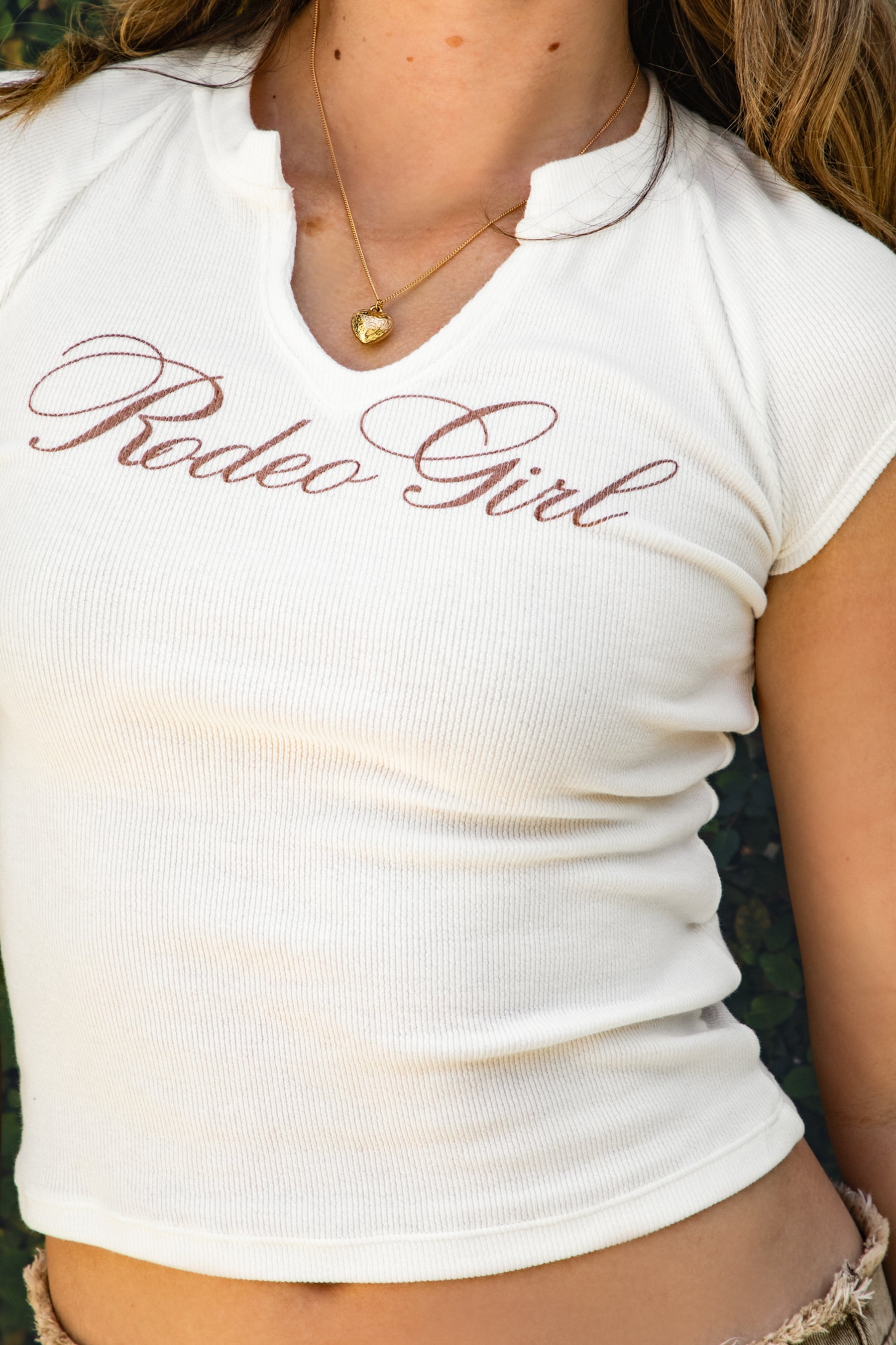 Woman wearing LASSO Rodeo Girl print V-neck crop top featuring a slim V-neckline, vintage Rodeo Girl graphic screen print, cap sleeves, soft stretch jersey fabric, and a fitted cropped silhouette for western casual and denim styling.