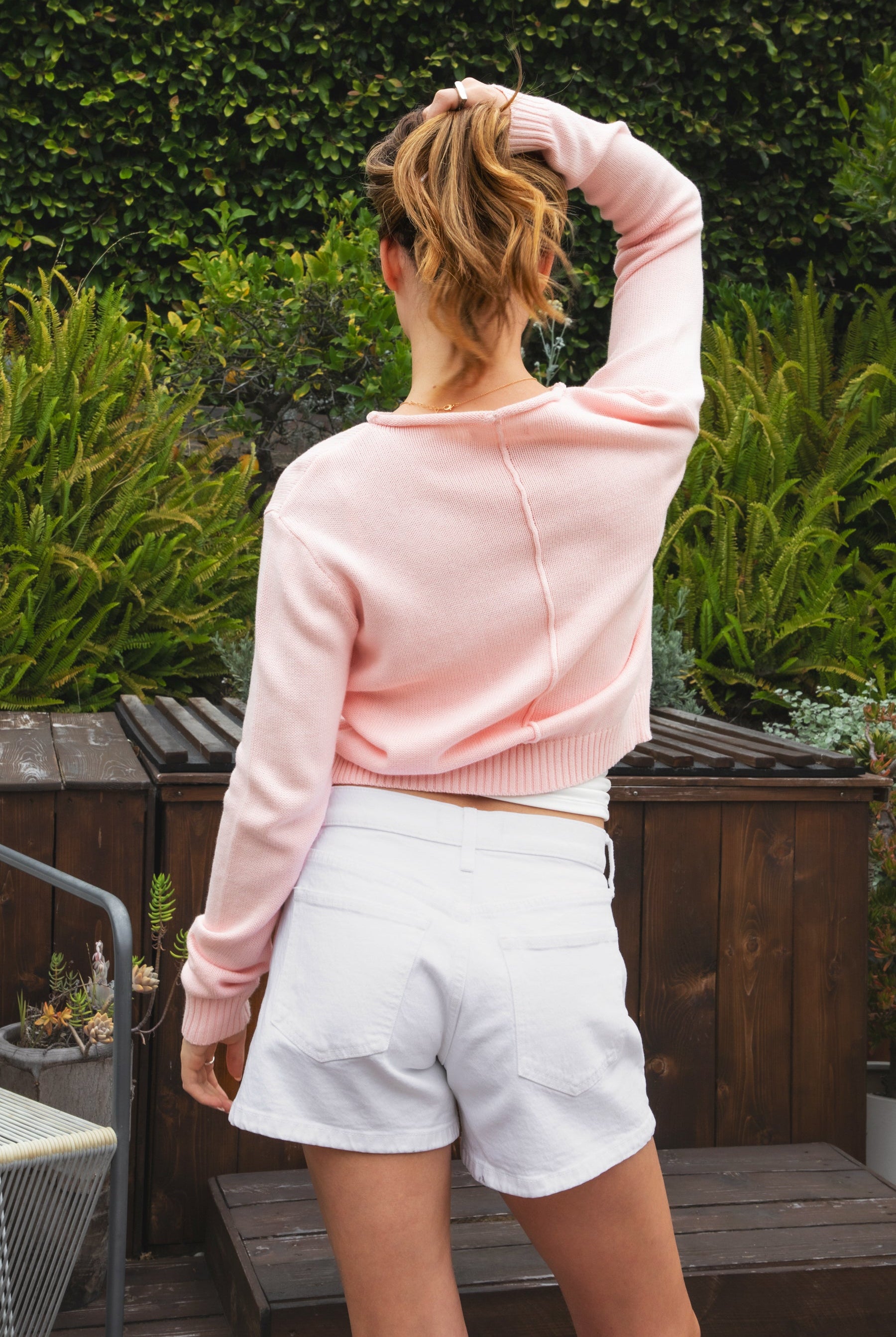Woman wearing LUMEE rolled neck long sleeve knit sweater featuring a minimal rolled neckline, soft cotton knit fabric, long sleeves with ribbed cuffs and hem, center back seam detail, and a relaxed cropped fit for easy everyday layering.