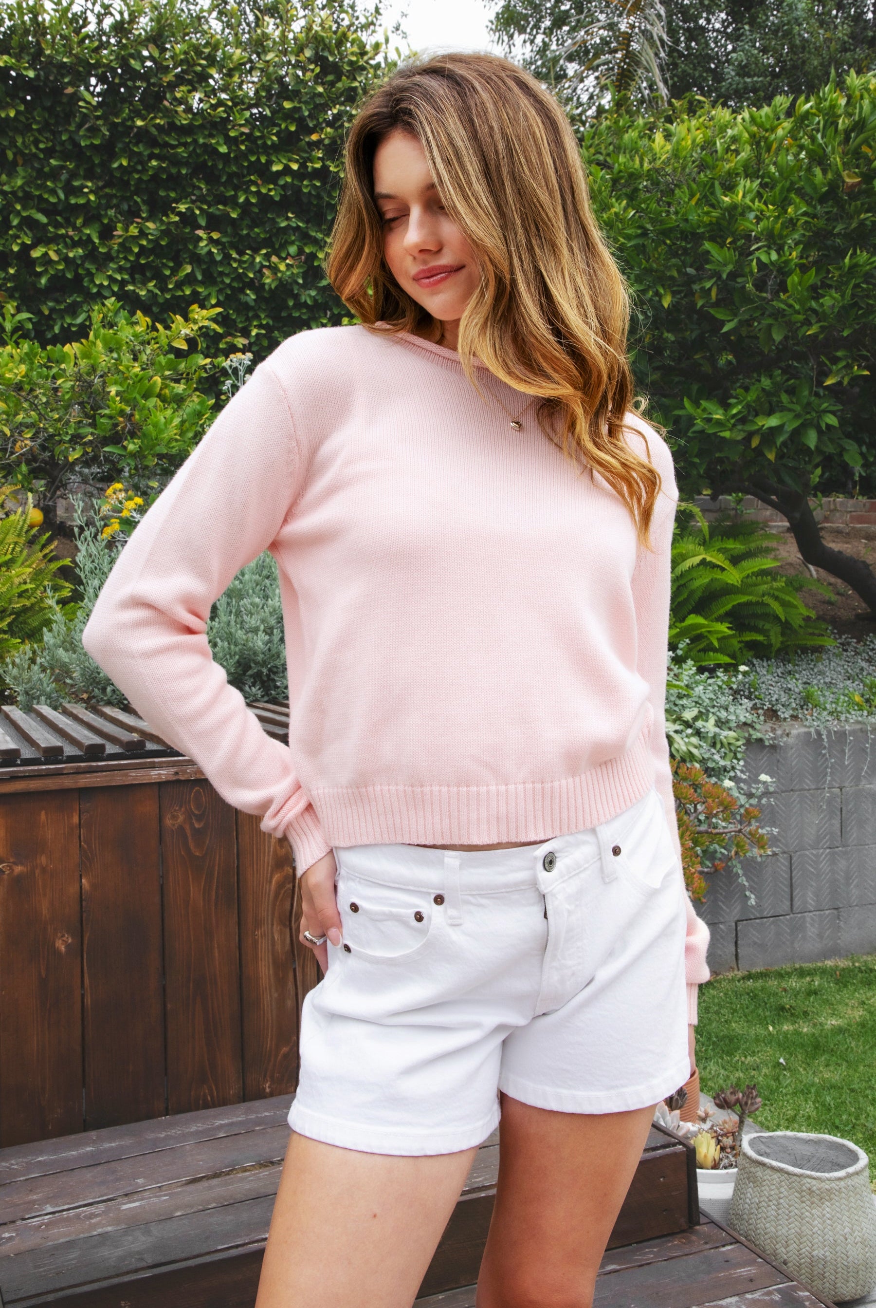 Woman wearing LUMEE rolled neck long sleeve knit sweater featuring a minimal rolled neckline, soft cotton knit fabric, long sleeves with ribbed cuffs and hem, center back seam detail, and a relaxed cropped fit for easy everyday layering.