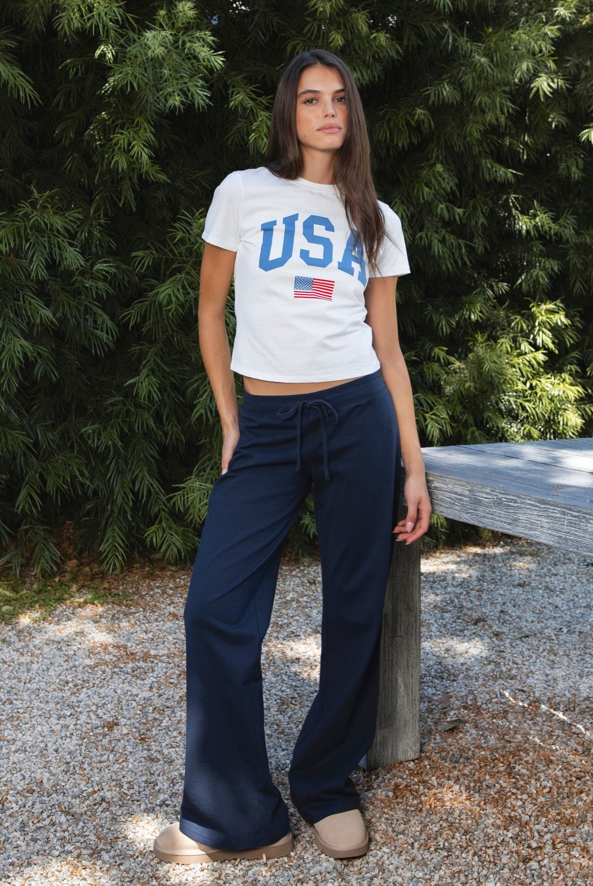 Woman wearing LIBERTY classic USA graphic crewneck baby tee featuring soft single jersey cotton stretch fabric, fitted short sleeve baby tee silhouette, clean cropped length, classic crew neckline, bold USA graphic across the front, American flag graphic detail below, and straight fitted hemline.