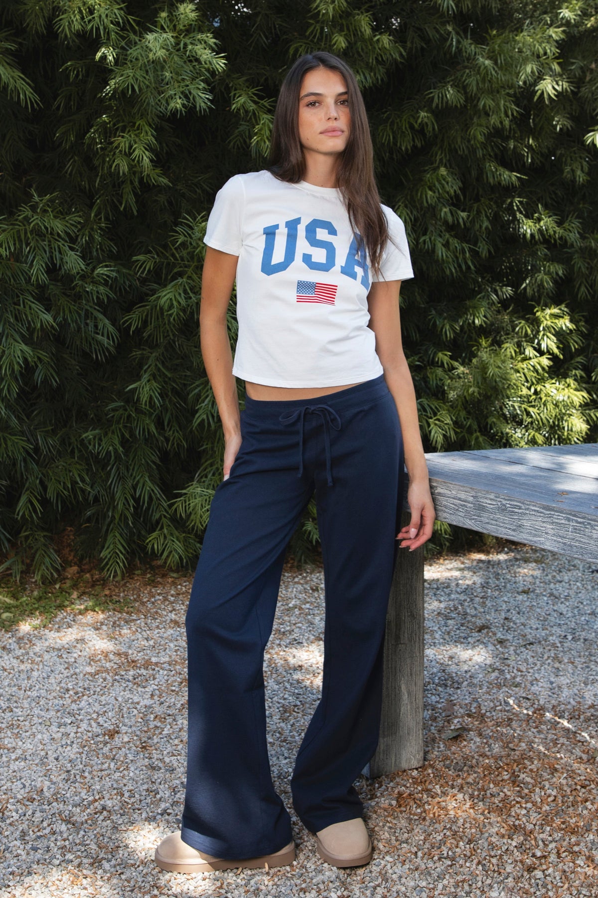 Woman wearing LIBERTY classic USA graphic crewneck baby tee featuring soft single jersey cotton stretch fabric, fitted short sleeve baby tee silhouette, clean cropped length, classic crew neckline, bold USA graphic across the front, American flag graphic detail below, and straight fitted hemline.