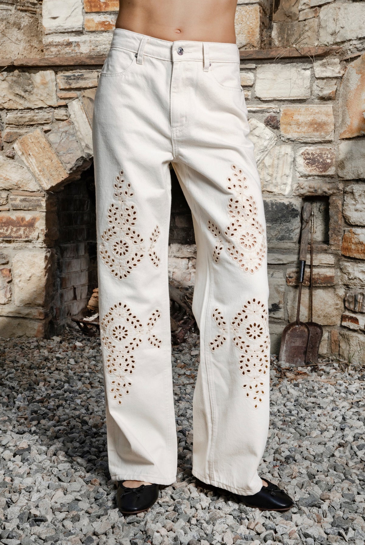 Woman wearing ALBA embroidered wide leg denim pants featuring structured cotton blend denim, high rise waist, classic four pocket design, intricate floral eyelet embroidery throughout the legs, relaxed wide leg silhouette, full length fit, button and zip fly closure, and belt loops along the waistline.
