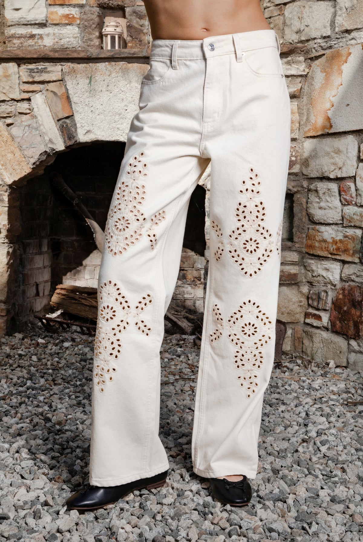 Woman wearing ALBA embroidered wide leg denim pants featuring structured cotton blend denim, high rise waist, classic four pocket design, intricate floral eyelet embroidery throughout the legs, relaxed wide leg silhouette, full length fit, button and zip fly closure, and belt loops along the waistline.
