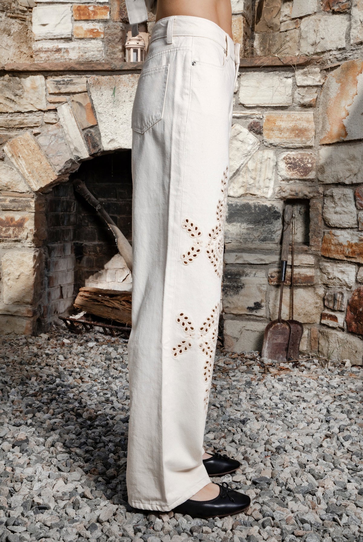 Woman wearing ALBA embroidered wide leg denim pants featuring structured cotton blend denim, high rise waist, classic four pocket design, intricate floral eyelet embroidery throughout the legs, relaxed wide leg silhouette, full length fit, button and zip fly closure, and belt loops along the waistline.