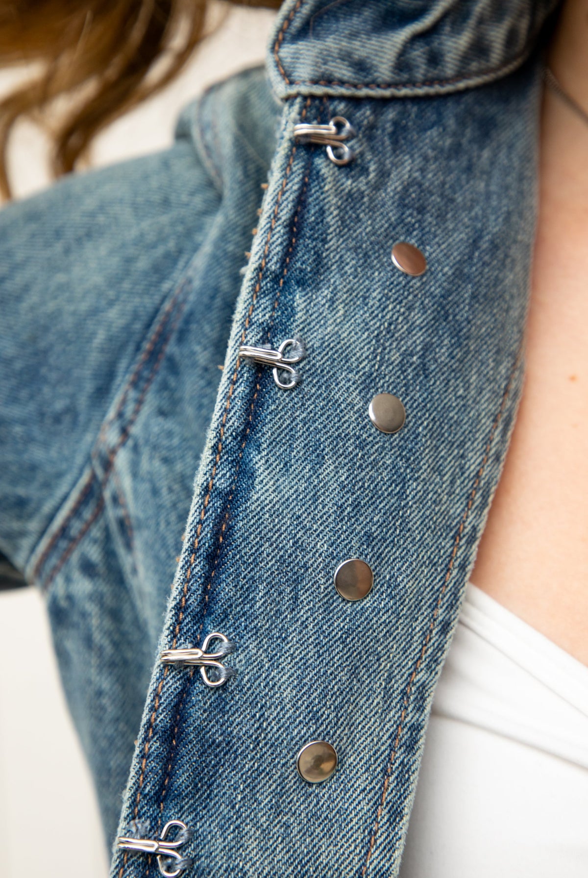 Woman wearing REMINGTON military semi crop denim jacket featuring cotton blend denim, structured tailored fit, military inspired horizontal strap panels, matte metal button accents, stand collar, hidden hook and eye front closure, long sleeves with metal button cuffs, and cropped hemline.