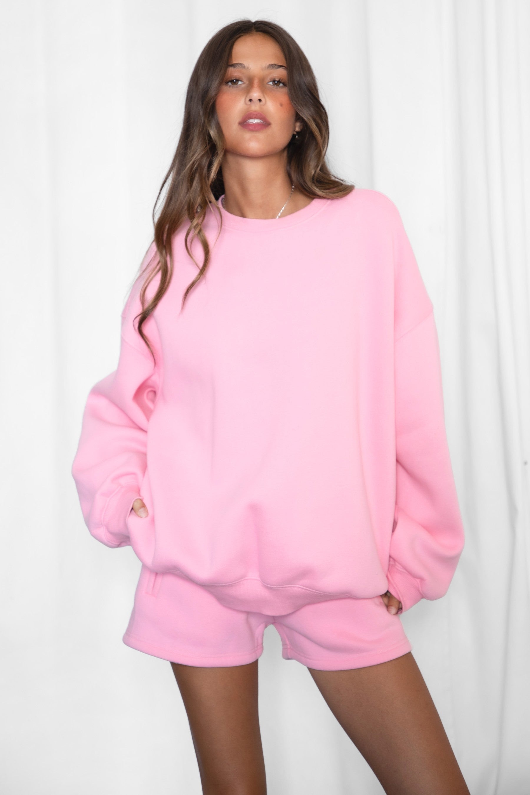 Person wearing a pink sweatshirt and shorts set on a white background