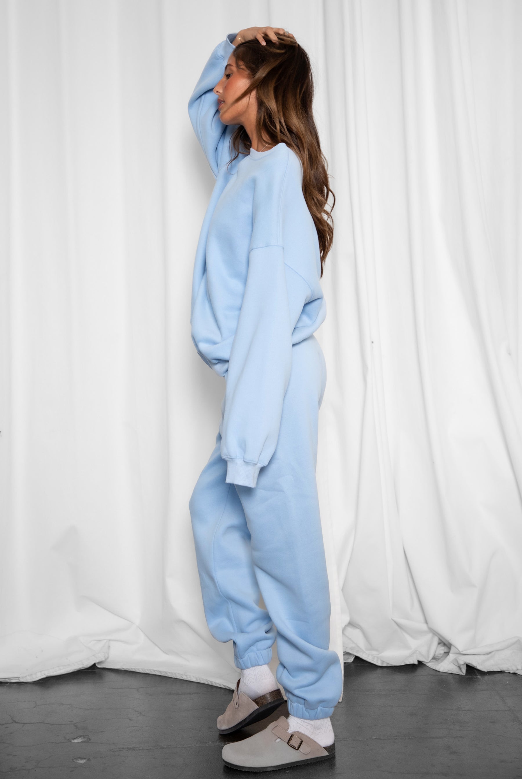 Person wearing a light blue tracksuit standing against a white curtain.