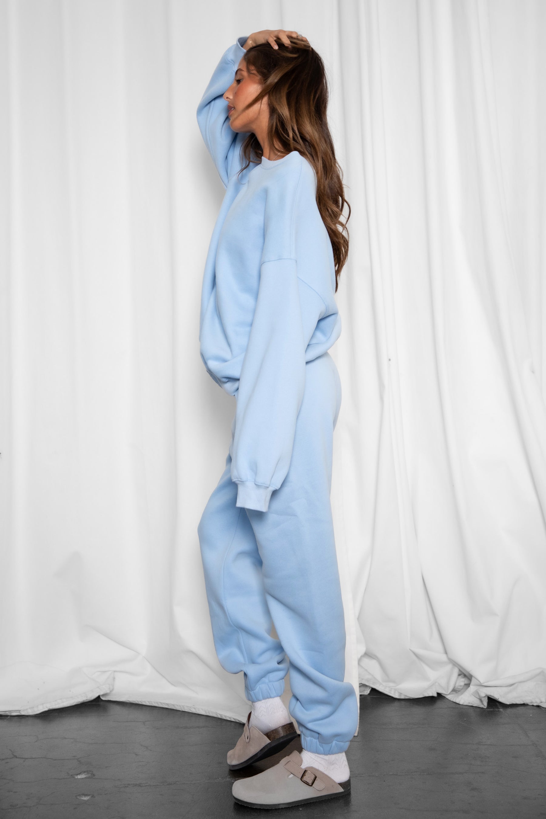 Person wearing a light blue tracksuit standing against a white curtain.