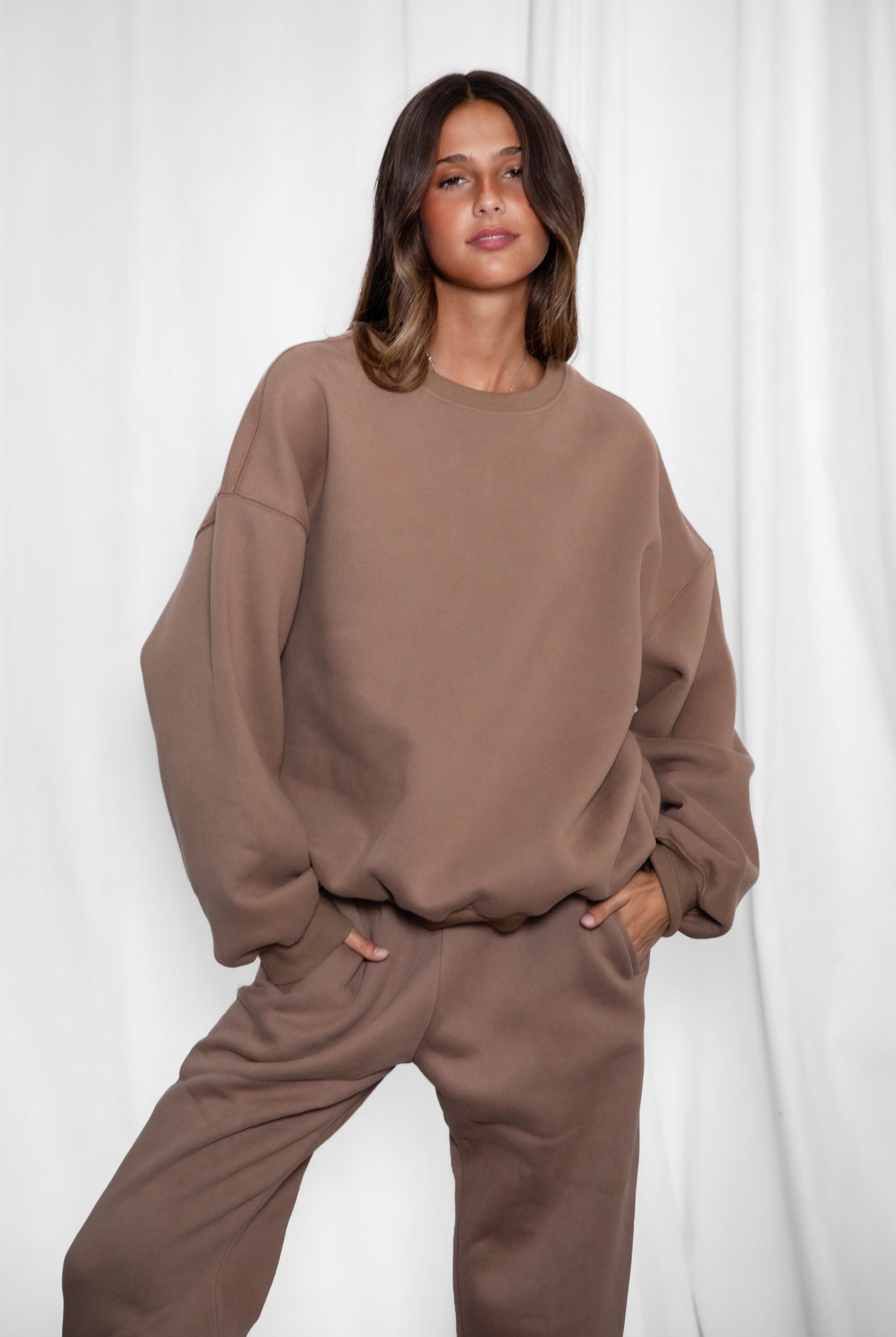 Person wearing a brown sweatshirt and pants against a white background