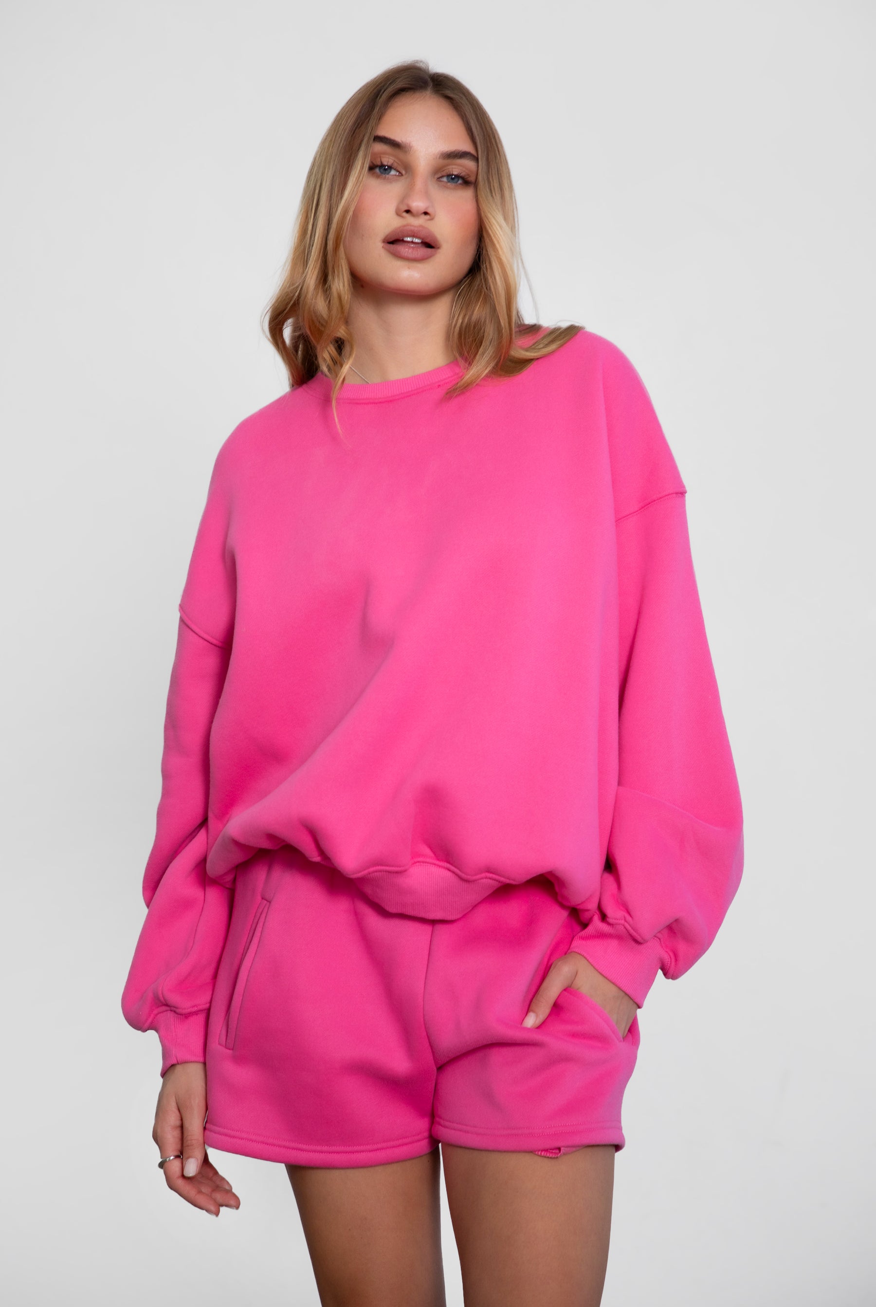 Person wearing a bright pink sweatshirt and shorts set on a white background