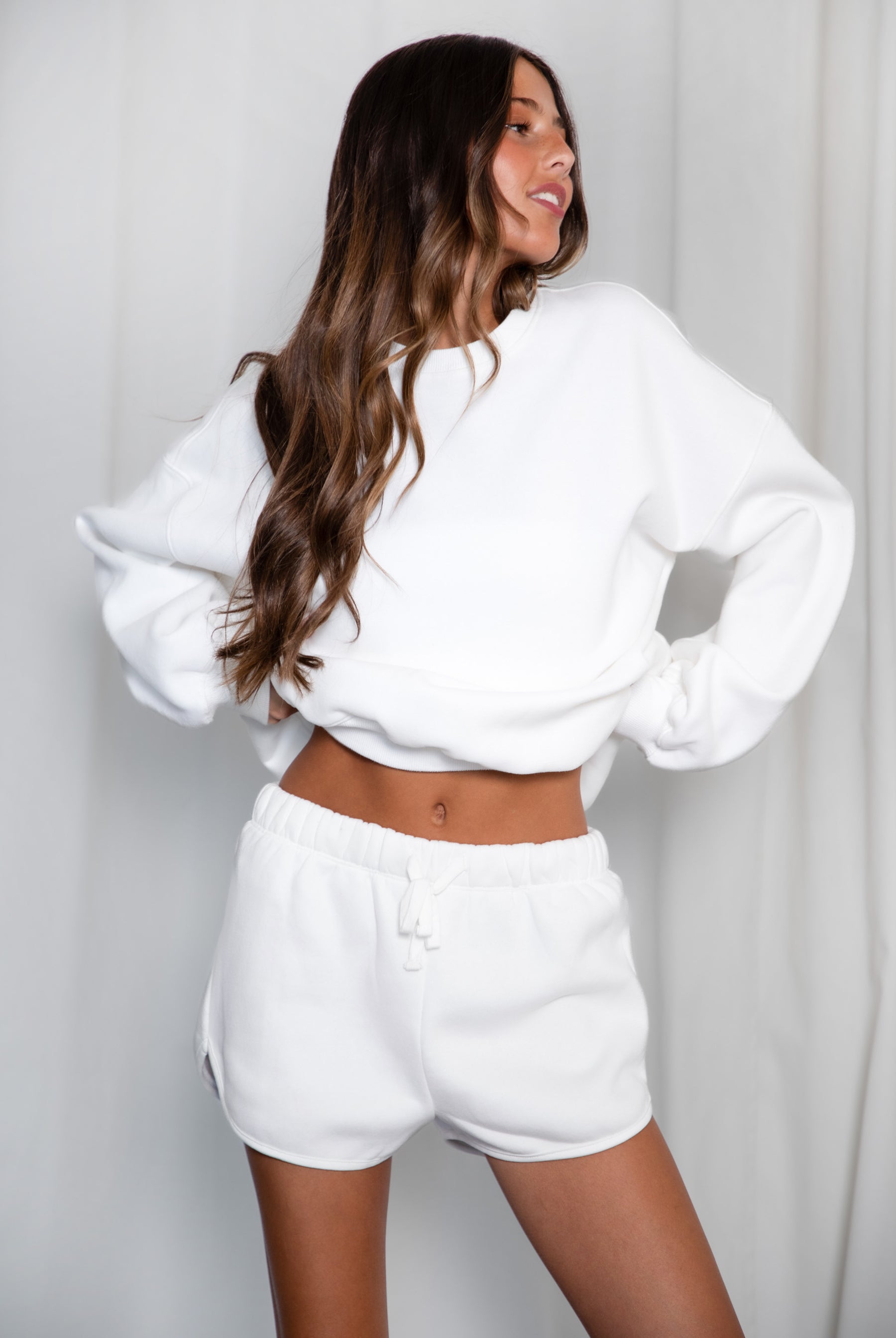 Woman wearing a white sweatshirt and shorts set against a plain background